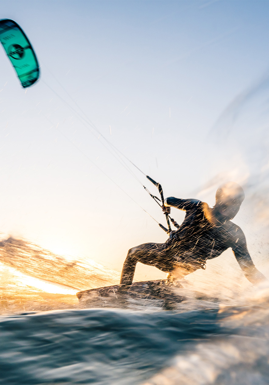 Hombre hace kitesurf en el mar con vela azul, agua salpicando y sol brillando