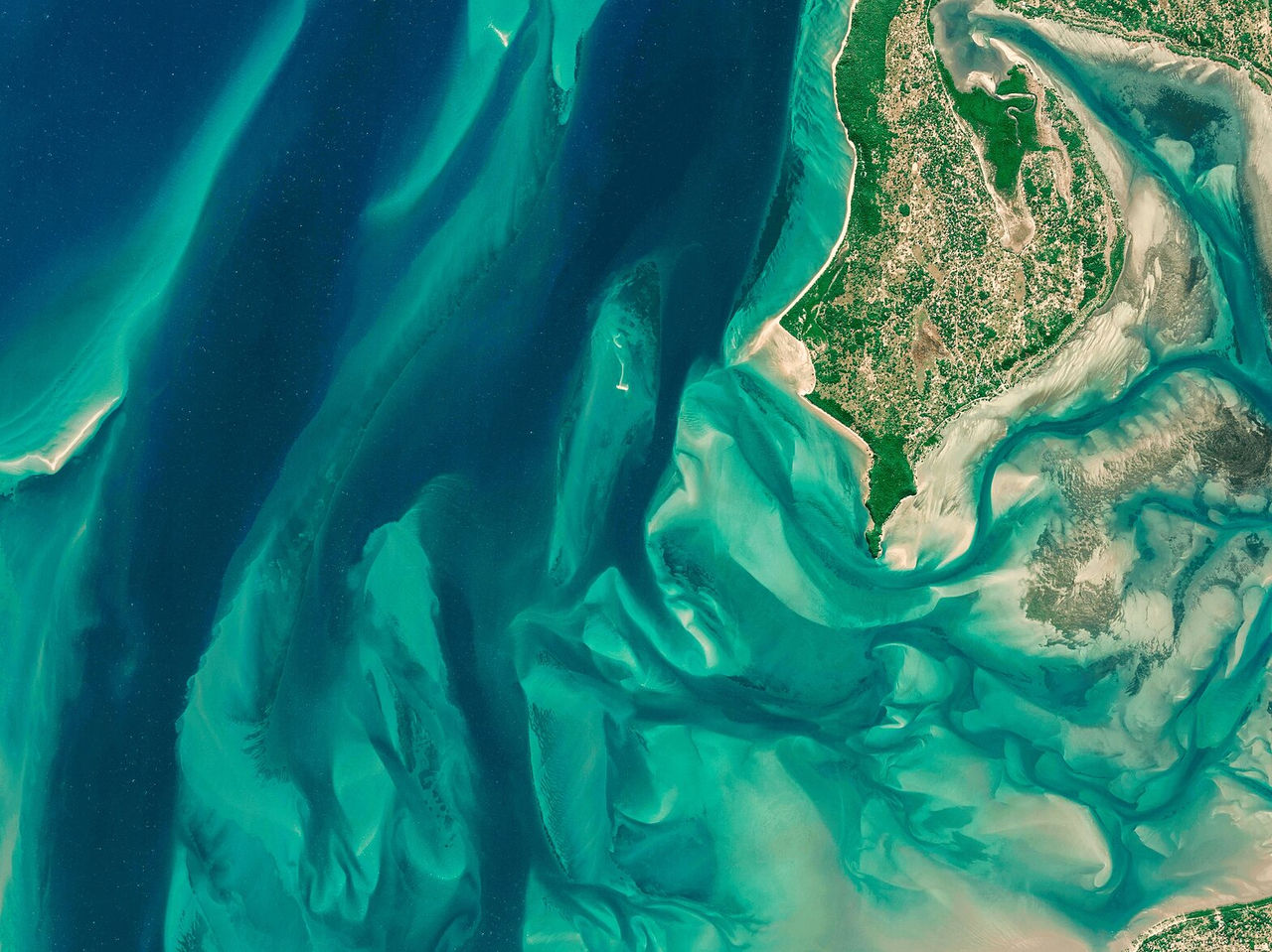 Vista aérea sobre planícies verdes e sobre o oceano, criando um padrão assimétrico de areia e água