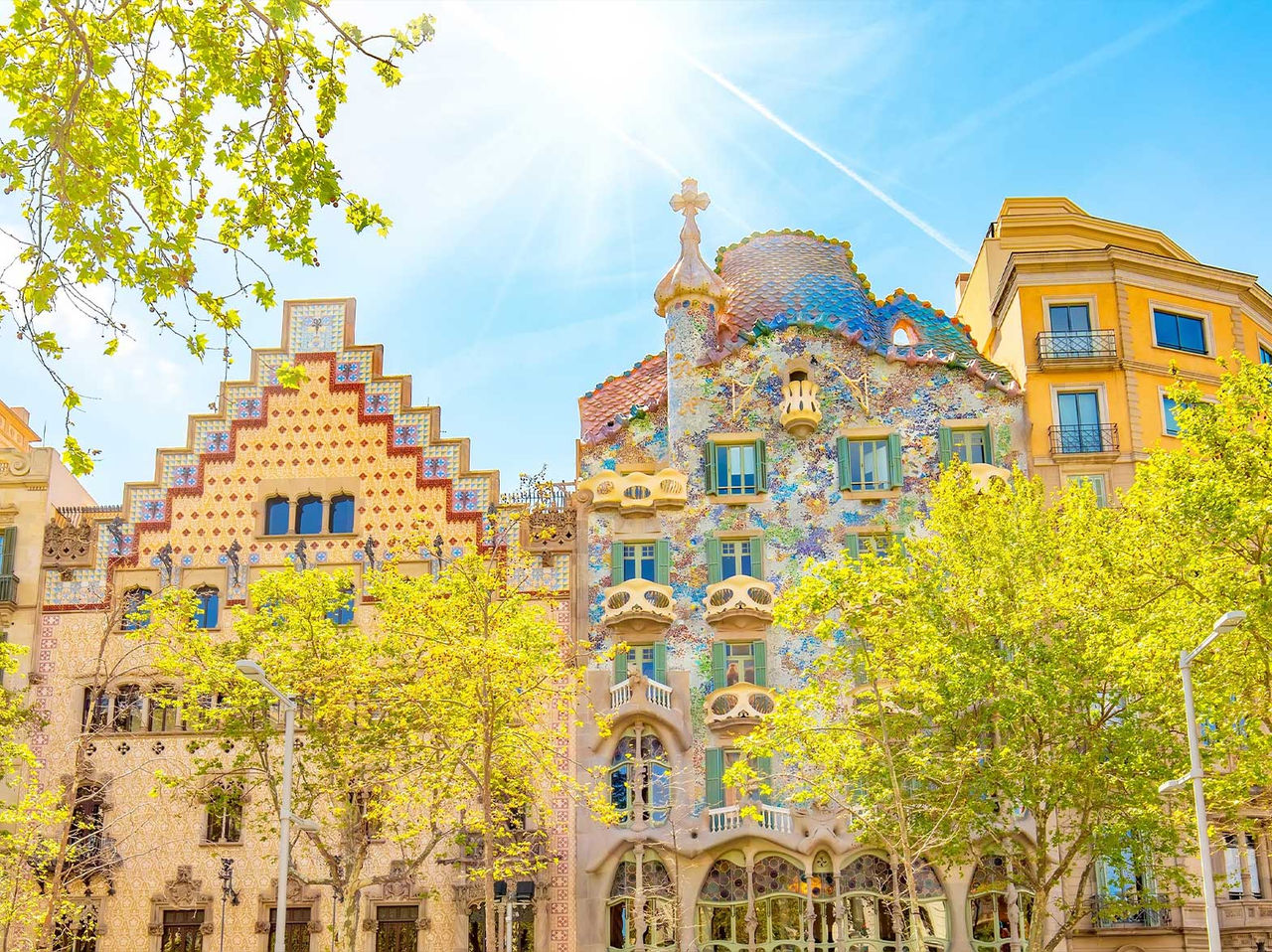 Icónico edifício da Casa Batlló de Gaudí, em Barcelona, com a sua fachada colorida, cercada por árvores floridas