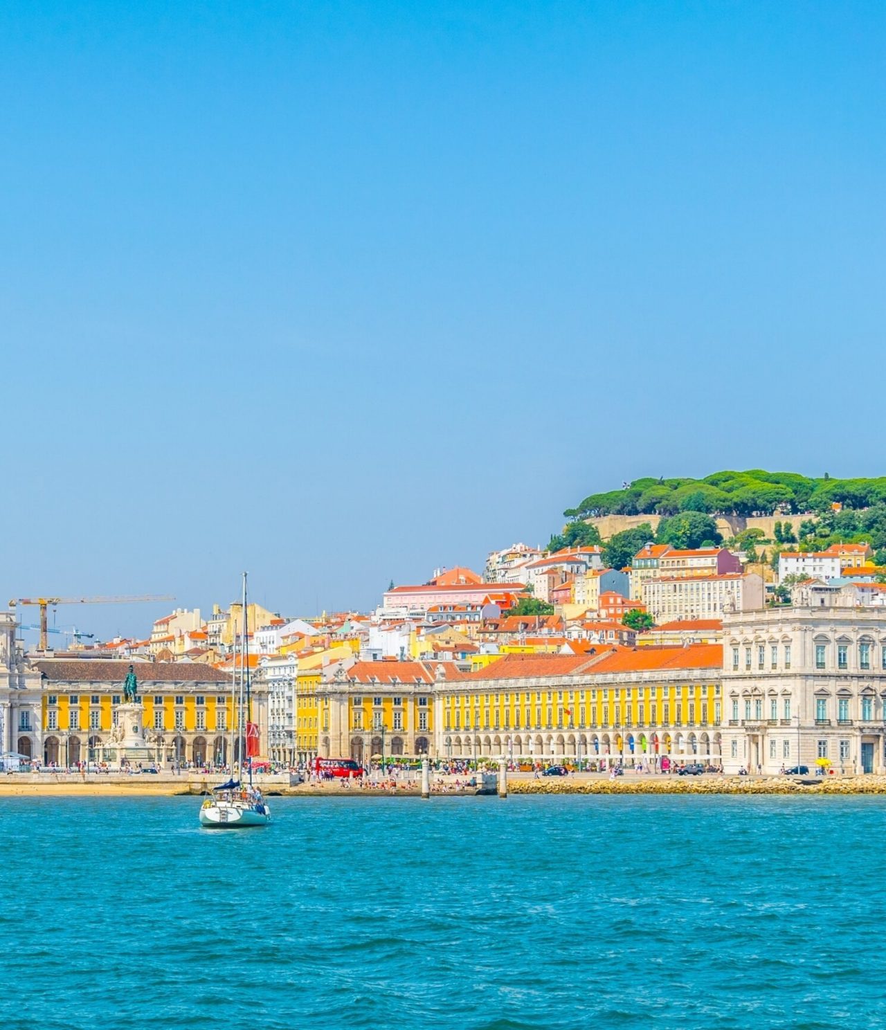 Vista do mar da cidade de Lisboa, com um veleiro na água, e o terreiro do paço ao fundo, rodeado pela baixa de Lisboa