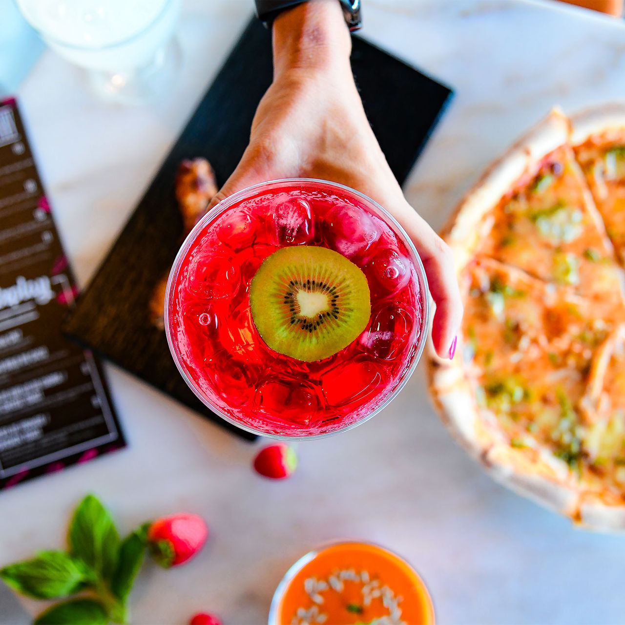 Vista de cima para um cocktail rosa com uma rodela de kiwi a acompanhar uma refeição de pizza no Pestana CR7 Funchal