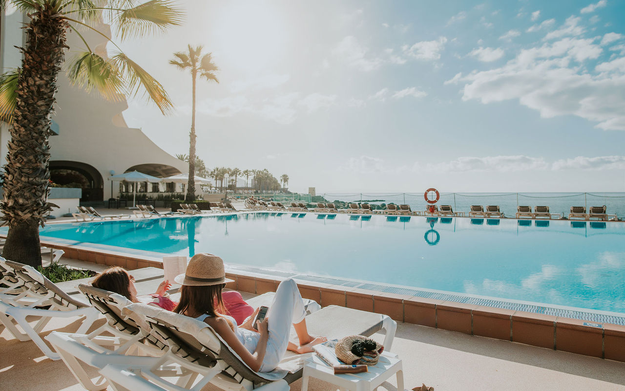 Pessoas a desfrutarem da piscina exterior com vista sobre o mar, de um hotel que pertence ao Pestana Hotels & Resorts