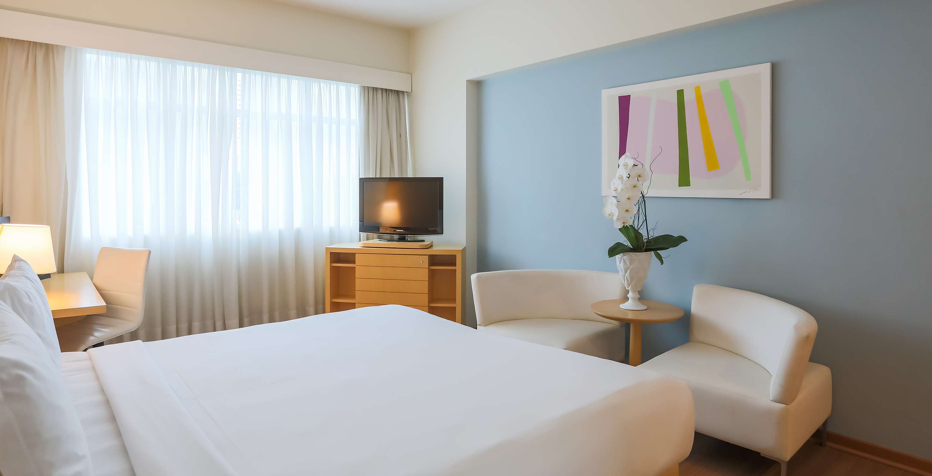 Der Deluxe-Eckzimmer im Pestana Curitiba hat ein Doppelbett, zwei Sofas, ein TV-Möbel und einen Schreibtisch