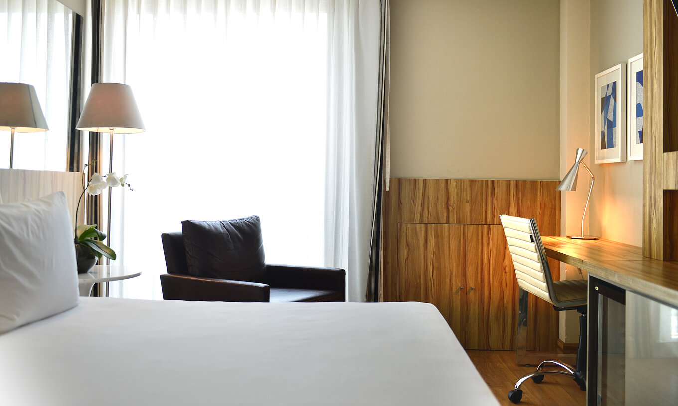 Das Zweibettzimmer mit Seitlichem Meerblick hat ein Doppelbett, einen Sessel und einen Schreibtisch mit Stuhl 