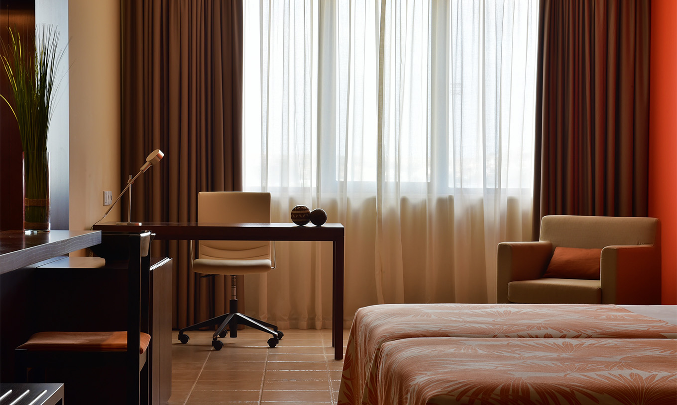 Standardzimmer Pestana Tropico hat einen Schreibtisch mit Lampe, einen Stuhl und einen Sessel