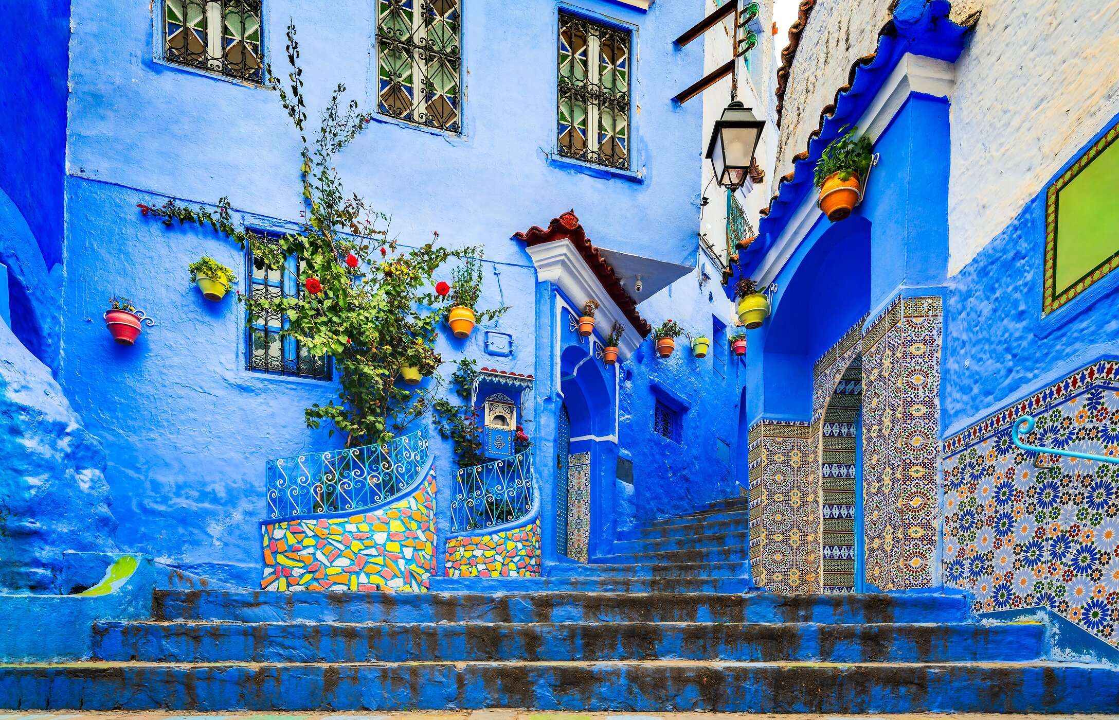 Treppe in Chefchaouen, mit blauen Gebäuden, Fliesenmustern und hängenden Töpfen.