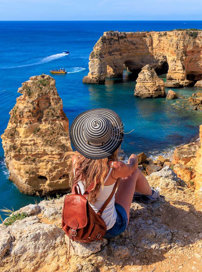Frau bewundert den Panoramablick auf die Algarve-Küste, mit kristallklarem Wasser und einer von Vegetation umgebenen Klippe