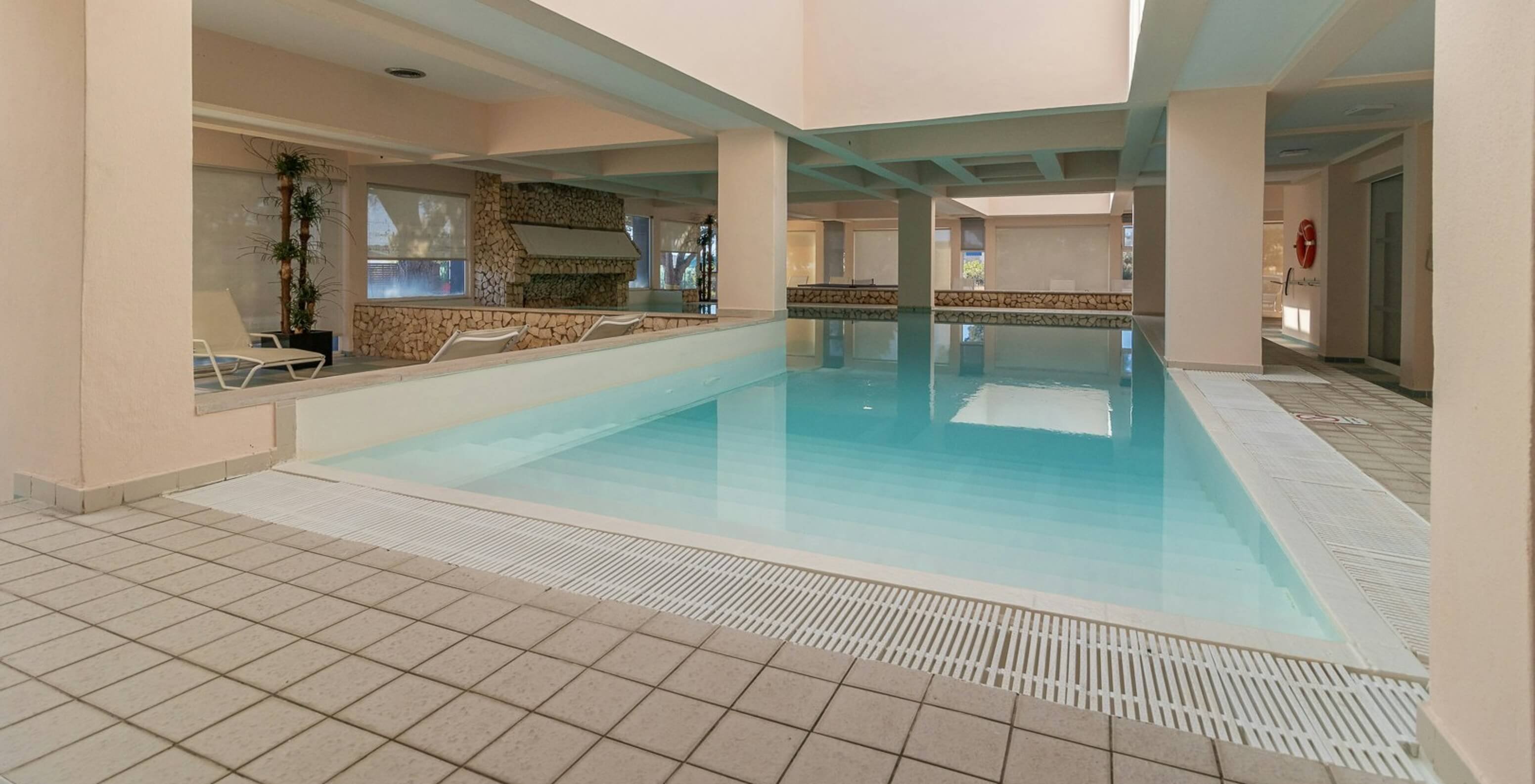 Innenpool mit natürlichem Licht und Liegen im Aparthotel am Meer