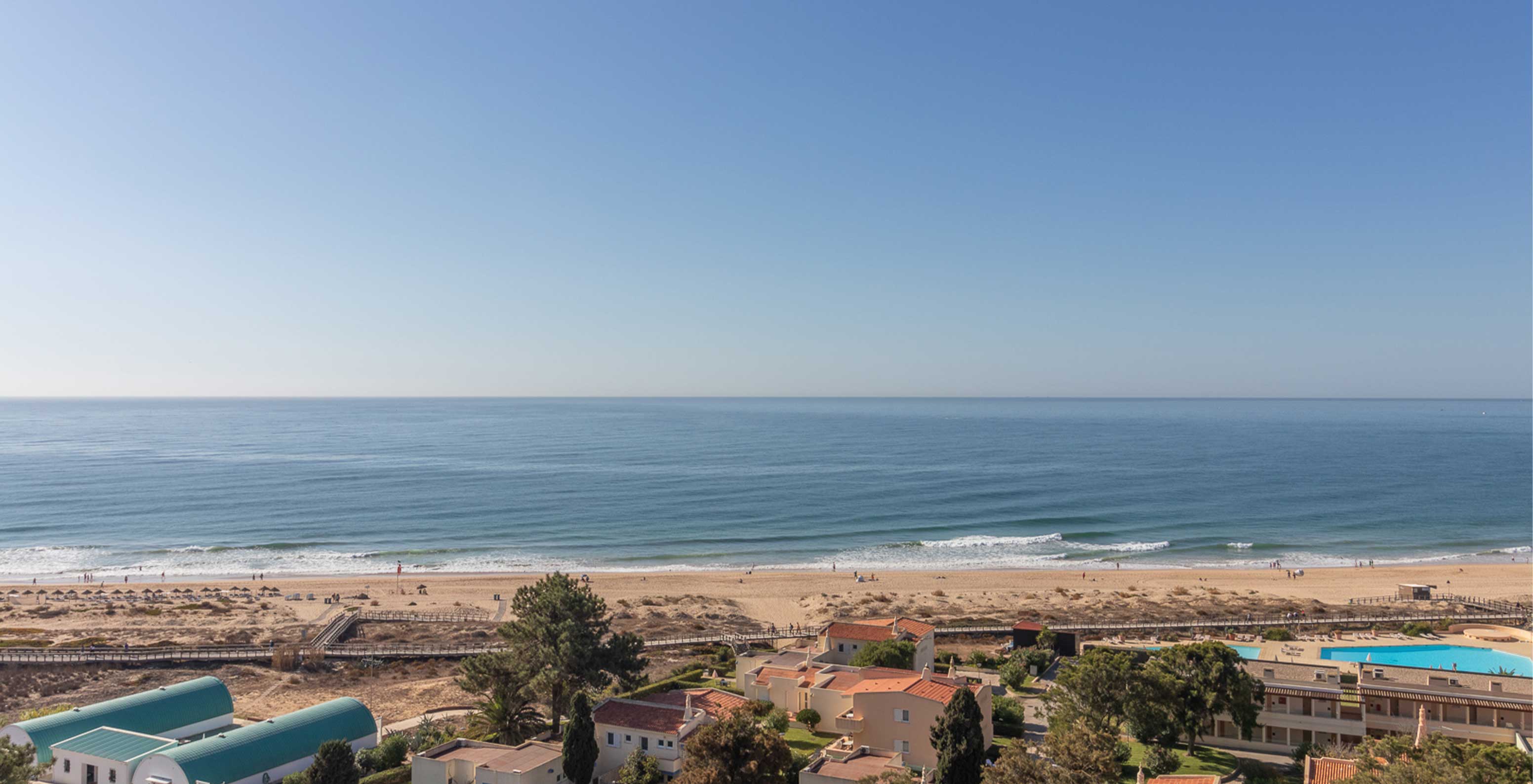 Der Strand von Alvor, Algarve, hat goldenen Sand und kristallklares Wasser, einen Steg und Dünen