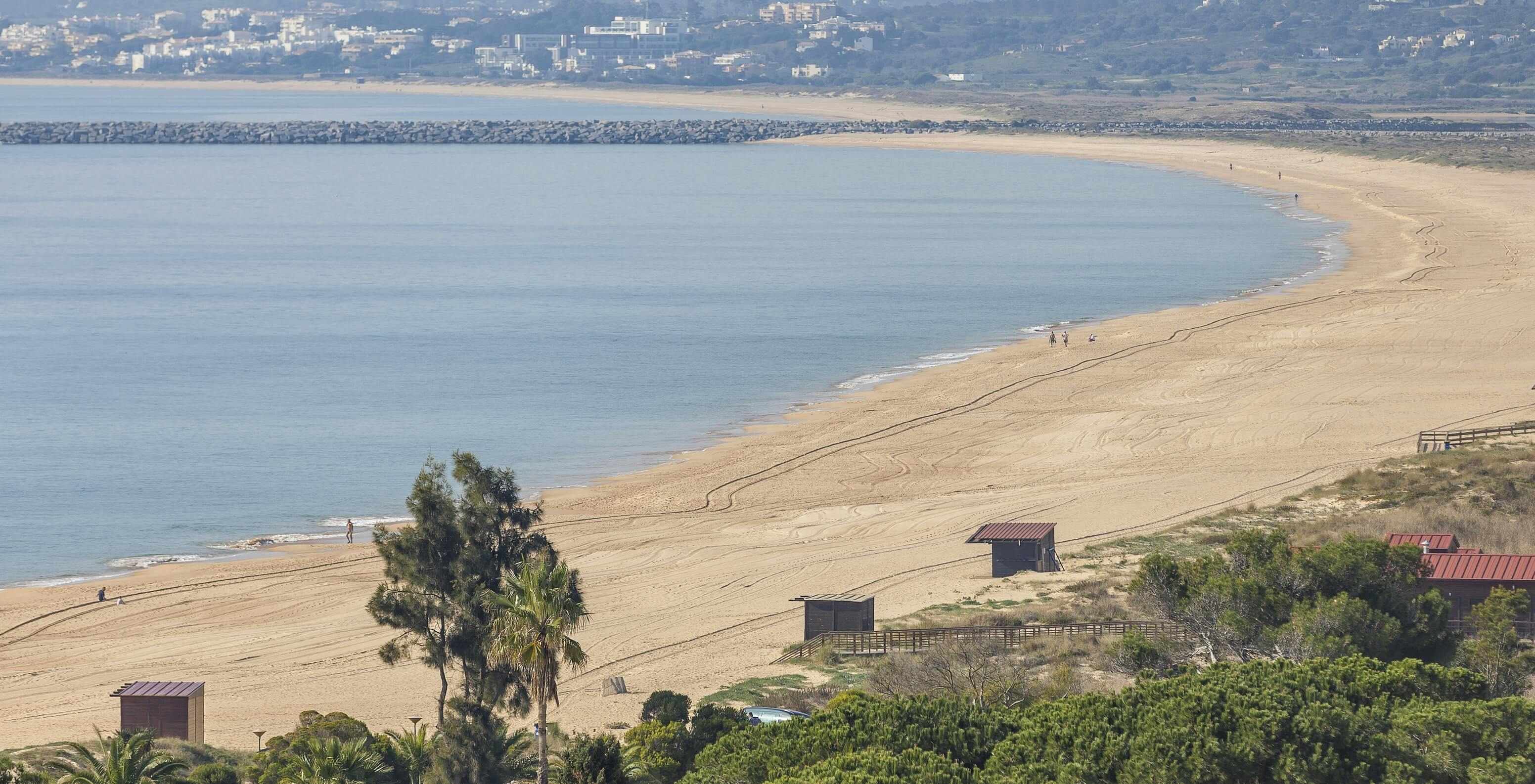 Der Strand von Alvor an der Algarve hat goldenen Sand, kristallklares Wasser, einen Steg und Dünen