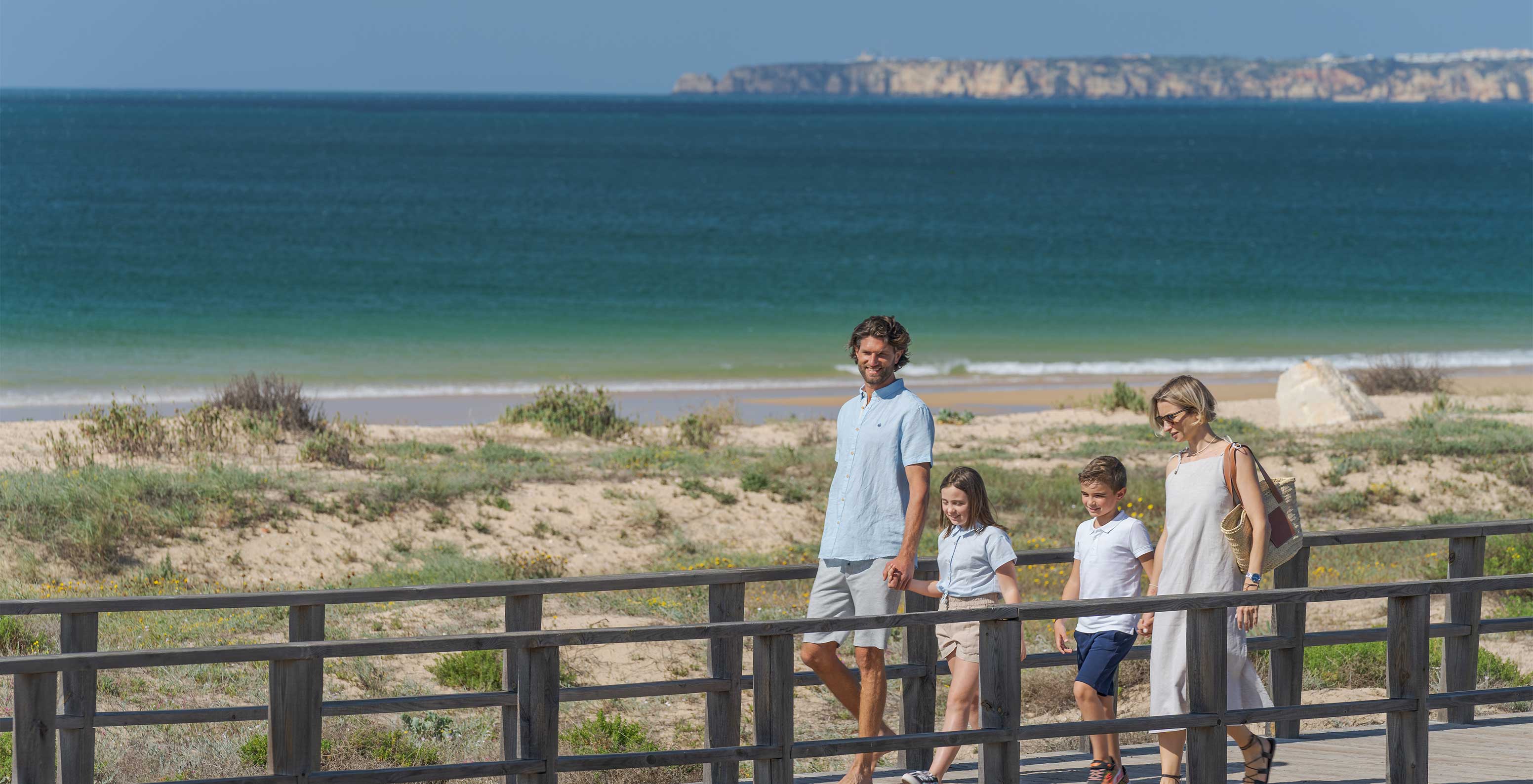 Familie spaziert lächelnd auf dem Steg am Strand von Alvor in der Algarve