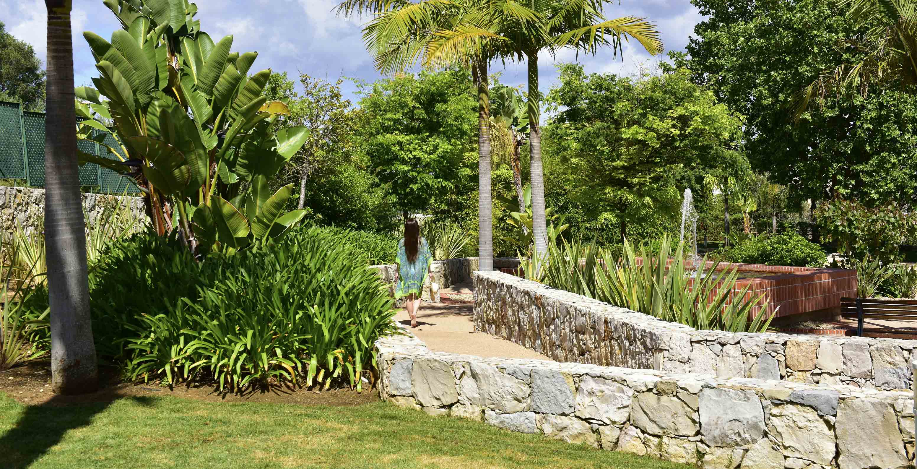 Gast spaziert im Garten mit tropischer Vegetation im Pestana Alvor Park, 4-Sterne-Aparthotel in Alvor mit Pool