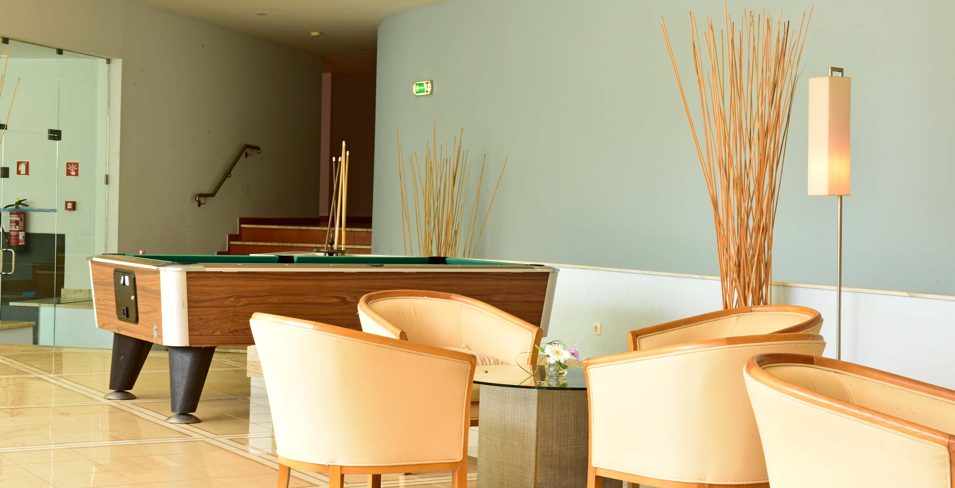 Spielzimmer mit Billardtisch, Stühlen und zentralem Tisch, mit Treppen im Hintergrund und Dekoration