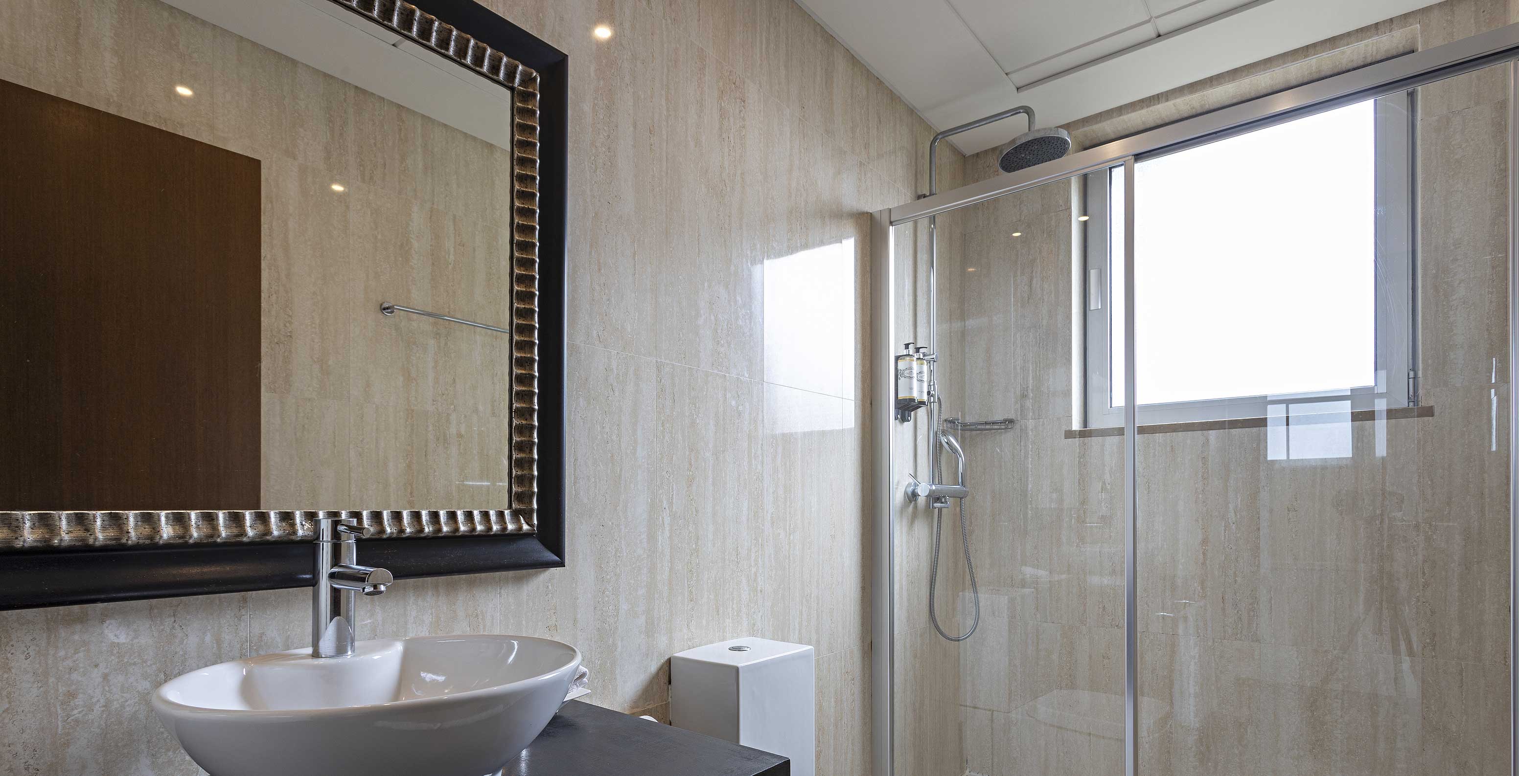 Die Cliff Suite T2 im Pestana Alvor Praia hat ein modernes Bad mit Fenster, Dusche, Waschbecken und Spiegel