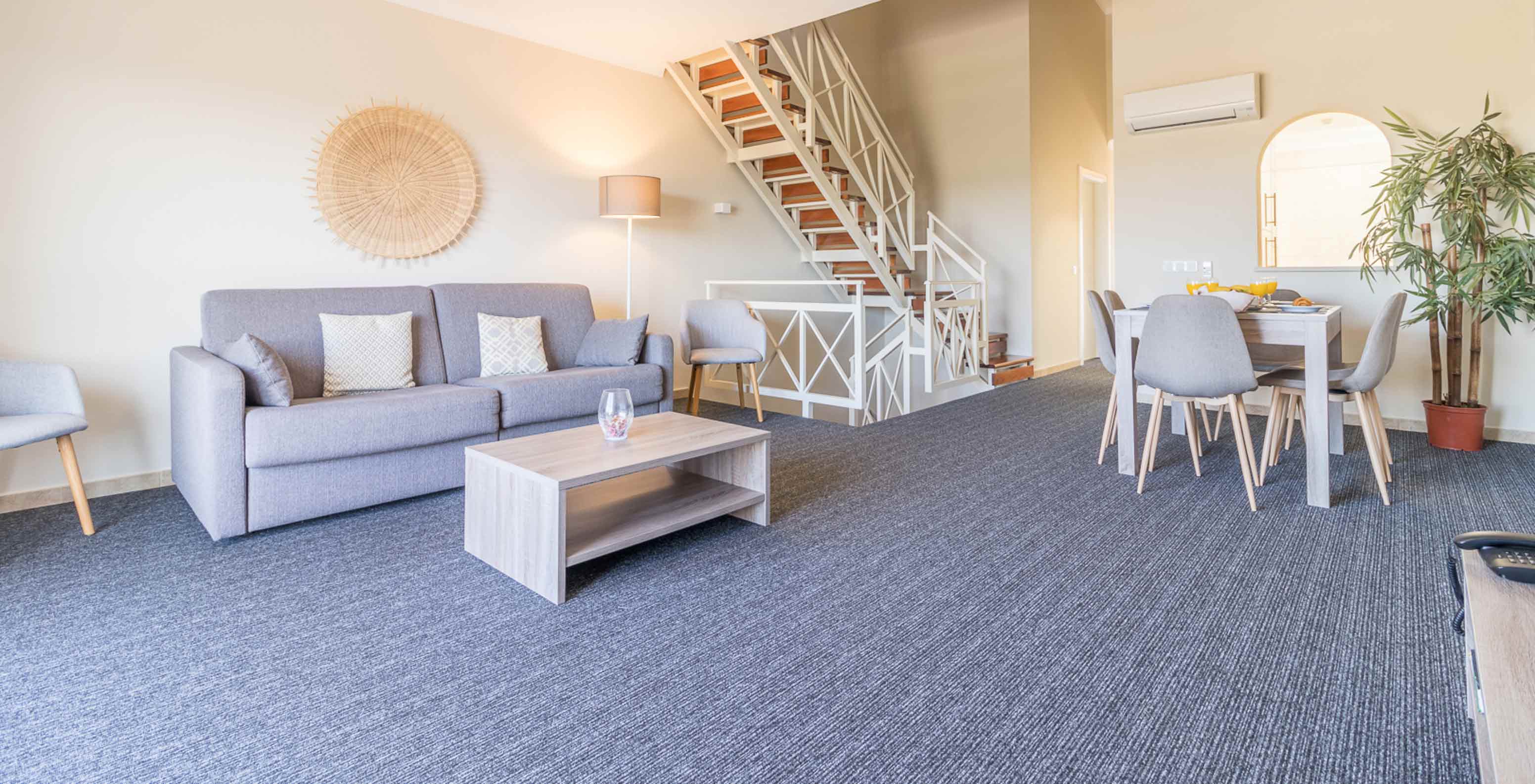 Das Zweizimmerapartment im Pestana Gramacho hat ein Wohnzimmer mit grauem Sofa, Tisch und Treppe im Hintergrund