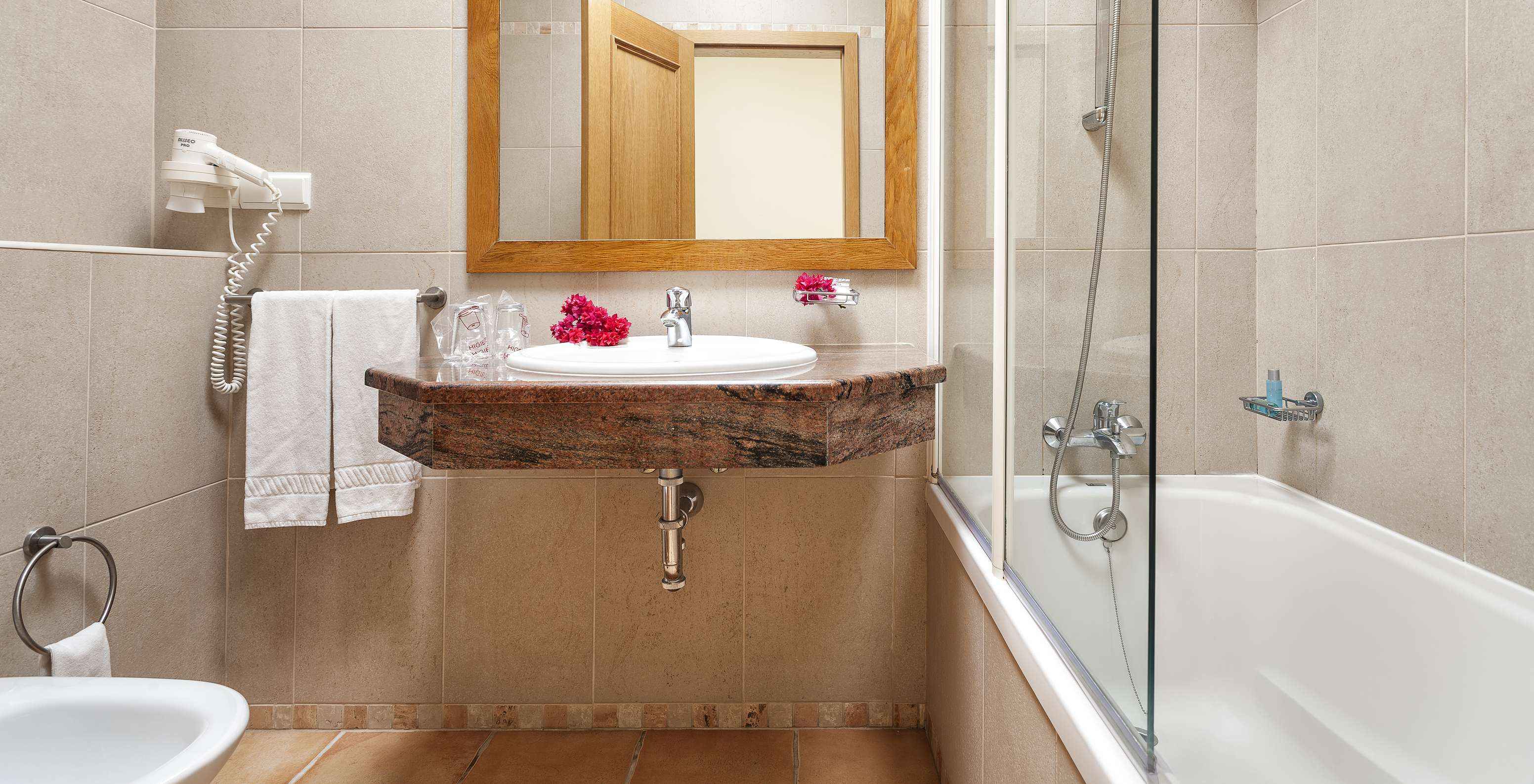 Das T1 Appartement - Terra im Pestana Palm Gardens hat eine Badewanne mit Dusche, ein Waschbecken mit Blumen und Spiegel