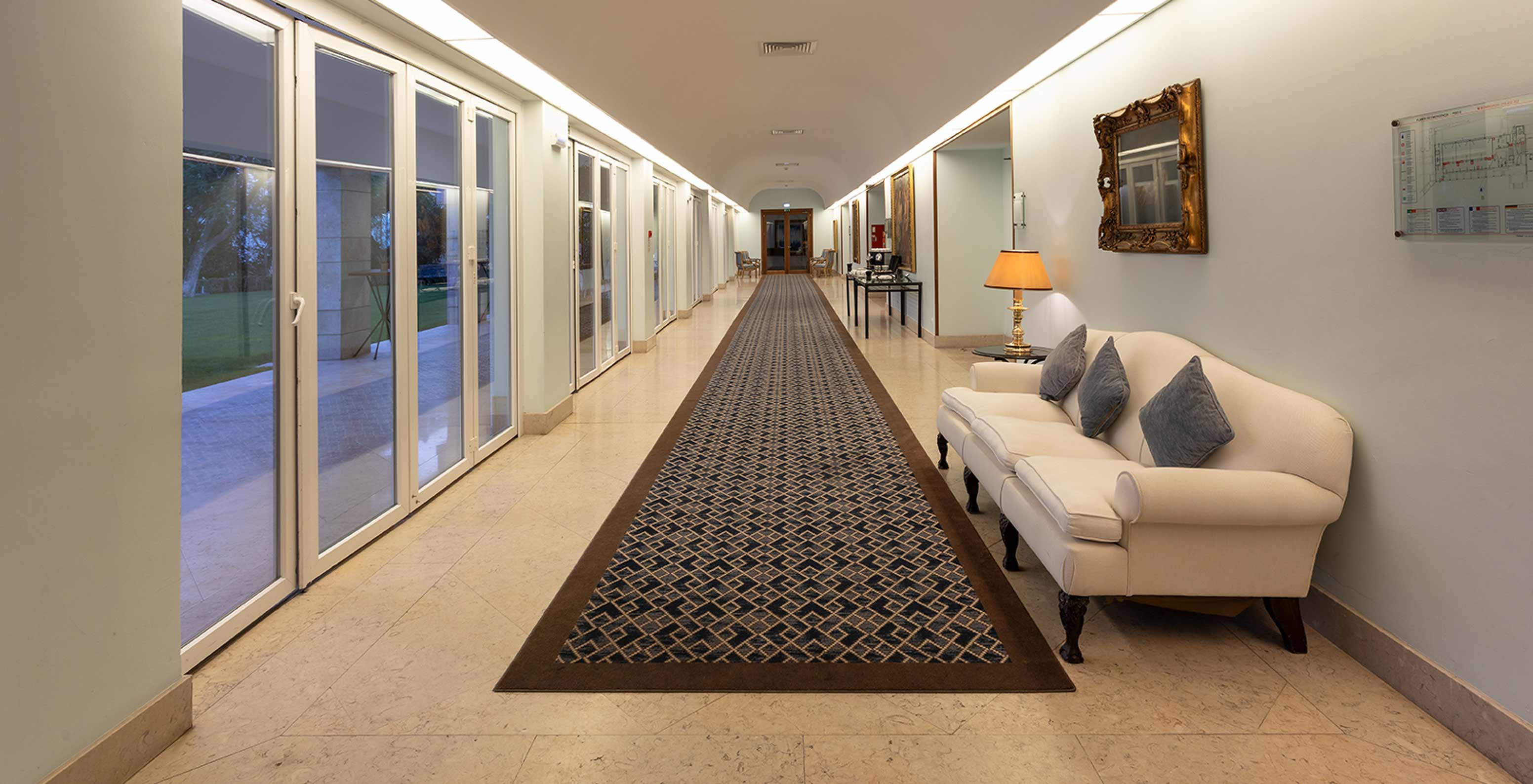 Das Pestana Palace Lisboa hat ein Foyer mit langem blauen Teppich, Sofa und großen Fenstern mit langen Vorhängen	