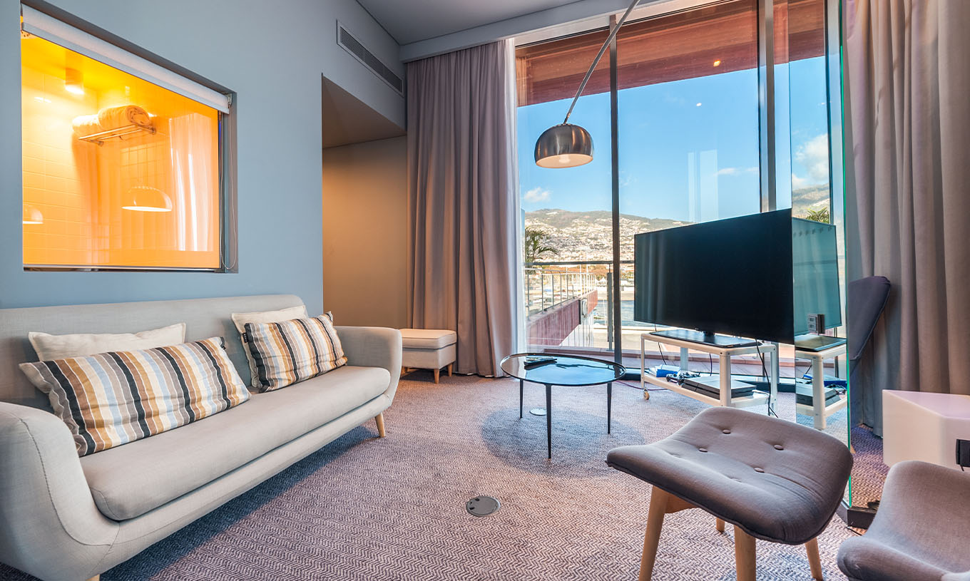 Die CR7 Suite im Pestana CR7 Funchal hat ein Wohnzimmer mit Sofa, Fernseher und Fenster mit Blick auf Funchal