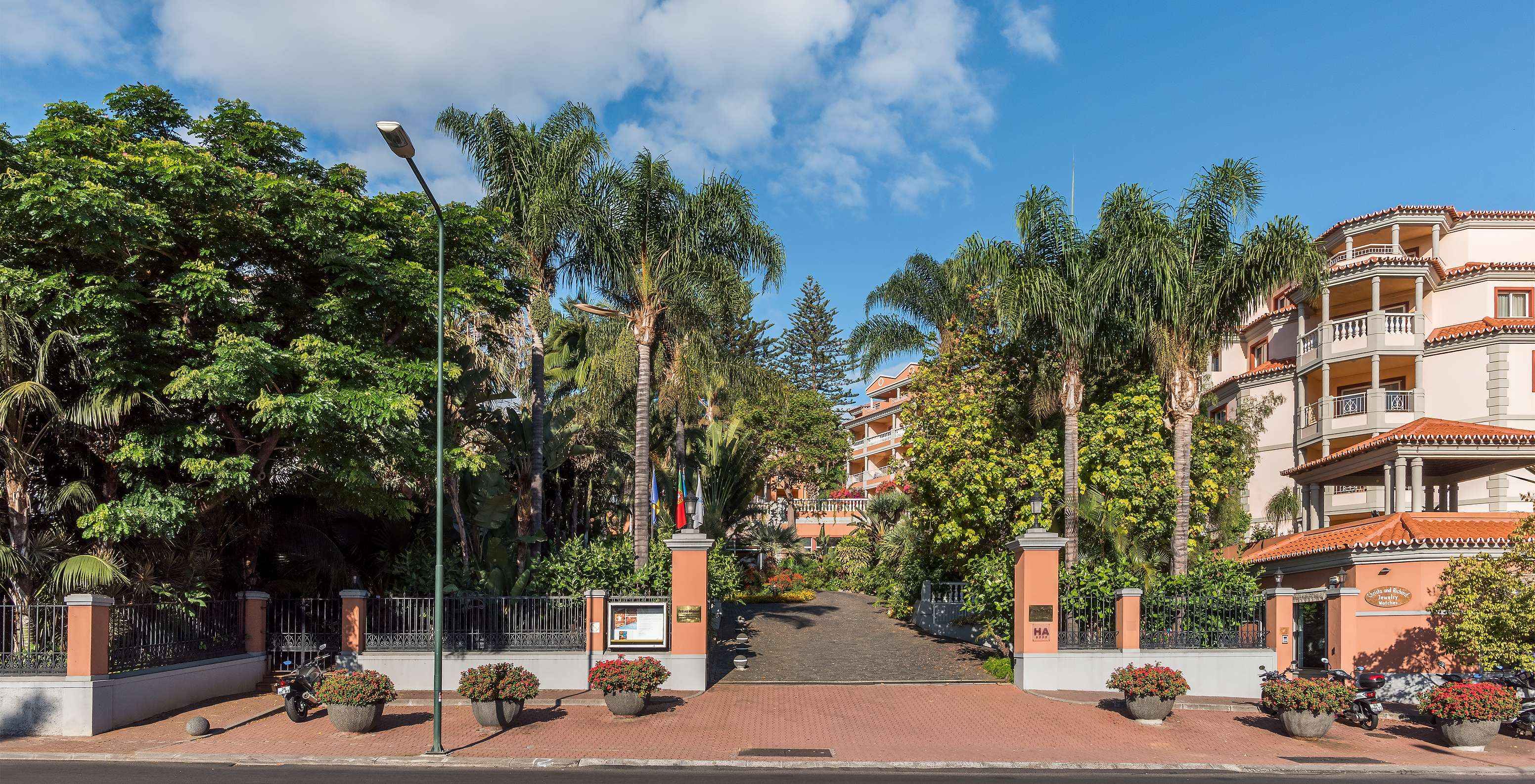 Eingang des Pestana Village, einem romantischen Hotel in Funchal, Madeira, mit mehreren Palmen und orangefarbenen Gebäuden