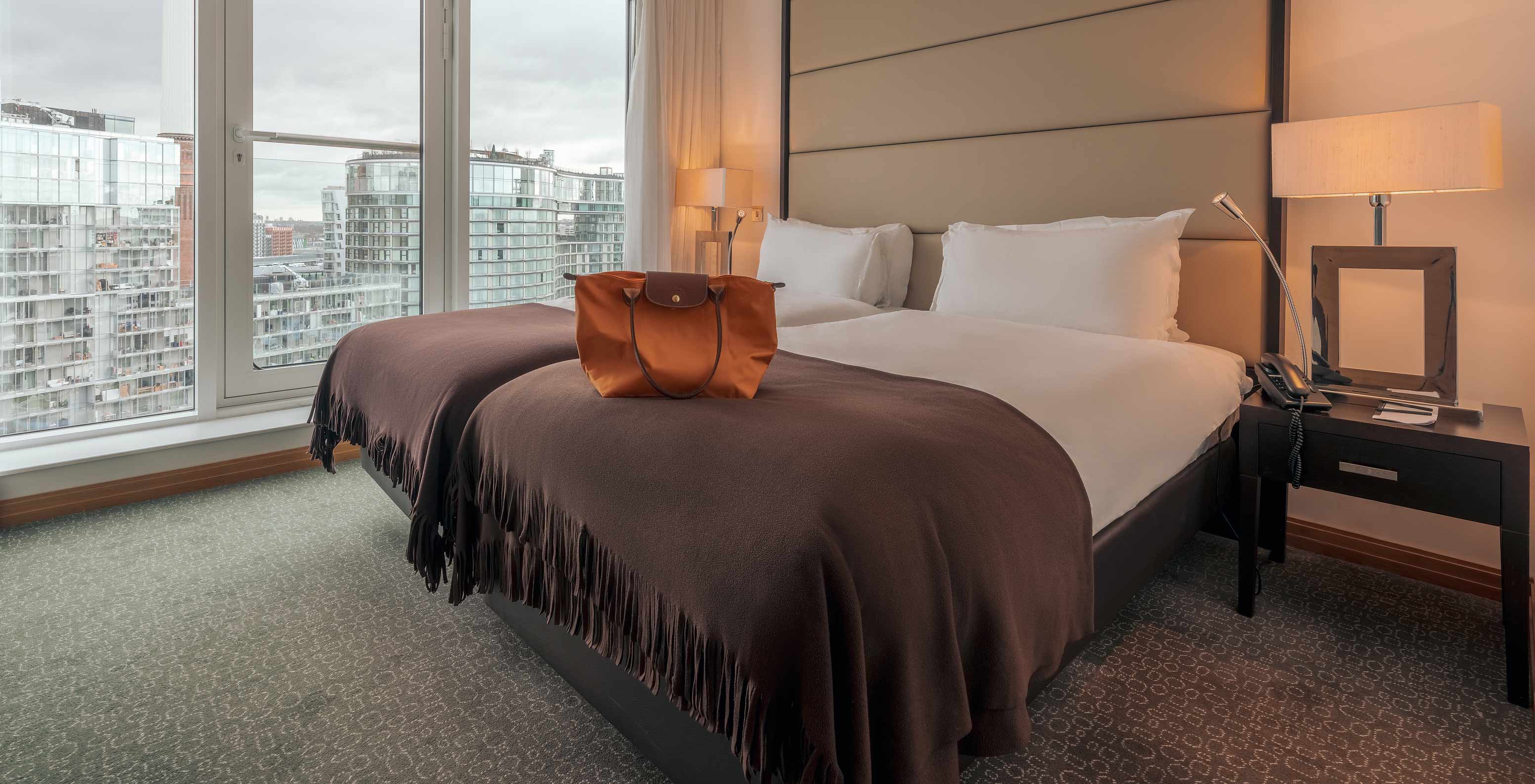 Das Superior Twin im Pestana Chelsea Bridge hat Doppelbett, Nachttische, Lampe und Fenster mit Stadtblick