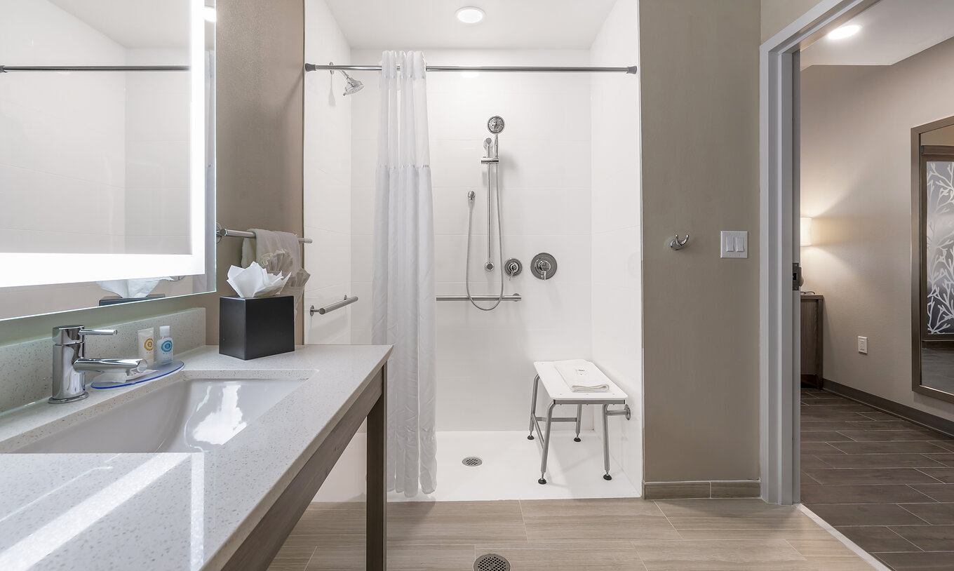 Die ADA King-Suite im Pestana Orlando Suites Lake Buena Vista hat ein Bad mit angepasster Dusche, Waschbecken und Spiegel