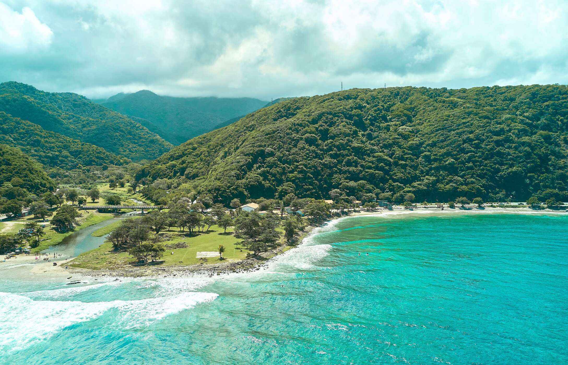 Luftaufnahme des Strandes La Punta in Venezuela, mit kristallklarem Wasser, umgeben von grünen Bergen.