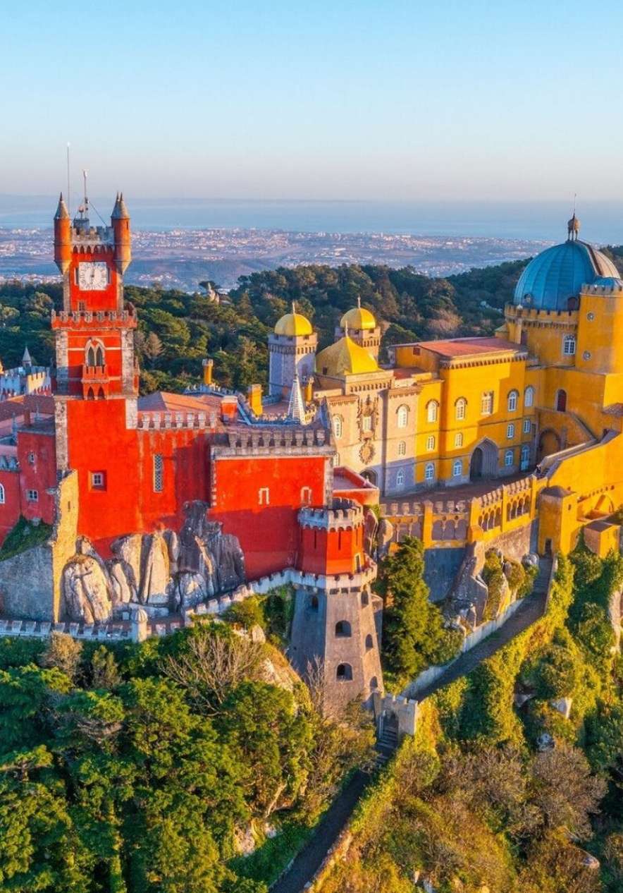 Panoramablick auf den Palast Pena in Sintra mit seinen roten und gelben Fassaden und dem Meer im Hintergrund