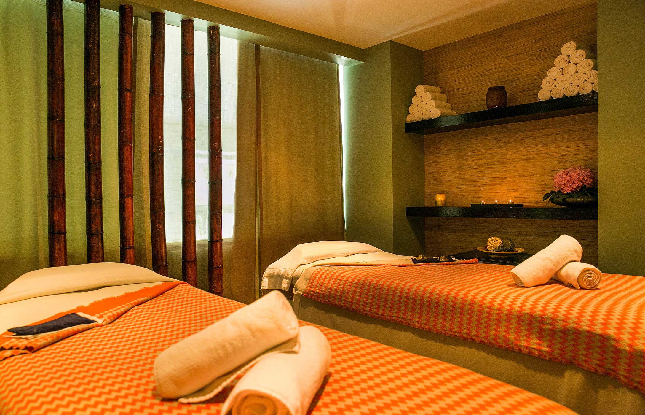 Entspannender Spa-Raum mit zwei Massageliegen, bedeckt mit orangefarbenen Decken, umgeben von Bambus, im Pestana Palace Spa