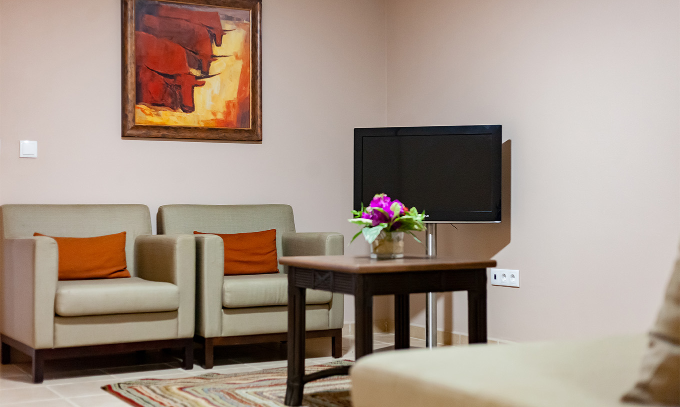 The Junior Suite at Pestana Tropico features two armchairs, a coffee table, and a television