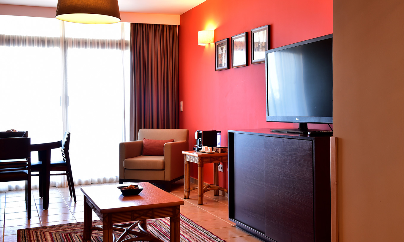 The Suite at Pestana Tropico features a living room with dining table, armchair, coffee table, and a television
