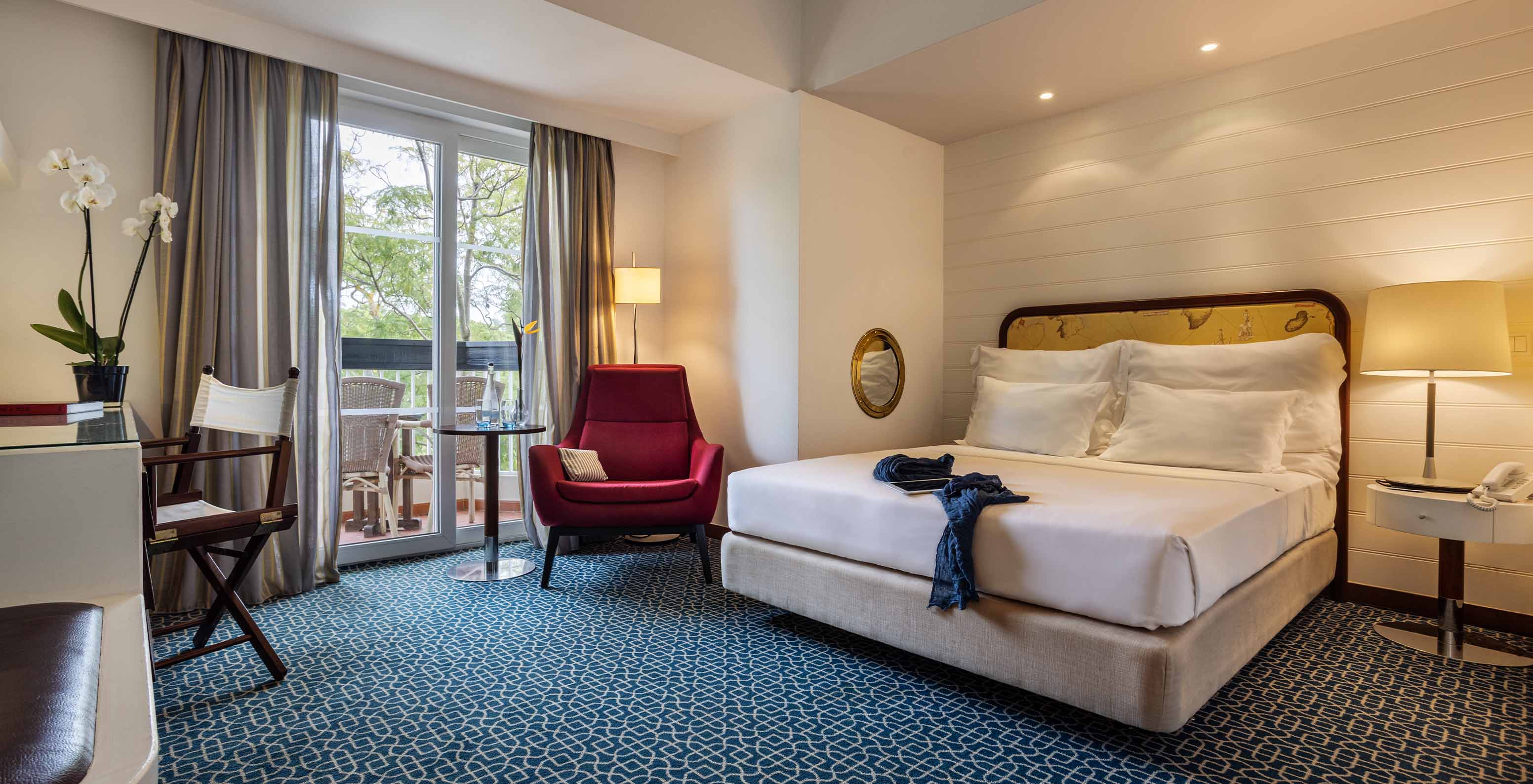 The Garden View Suite at Pestana Alvor Praia has a double bed, a red armchair, and a view with chairs