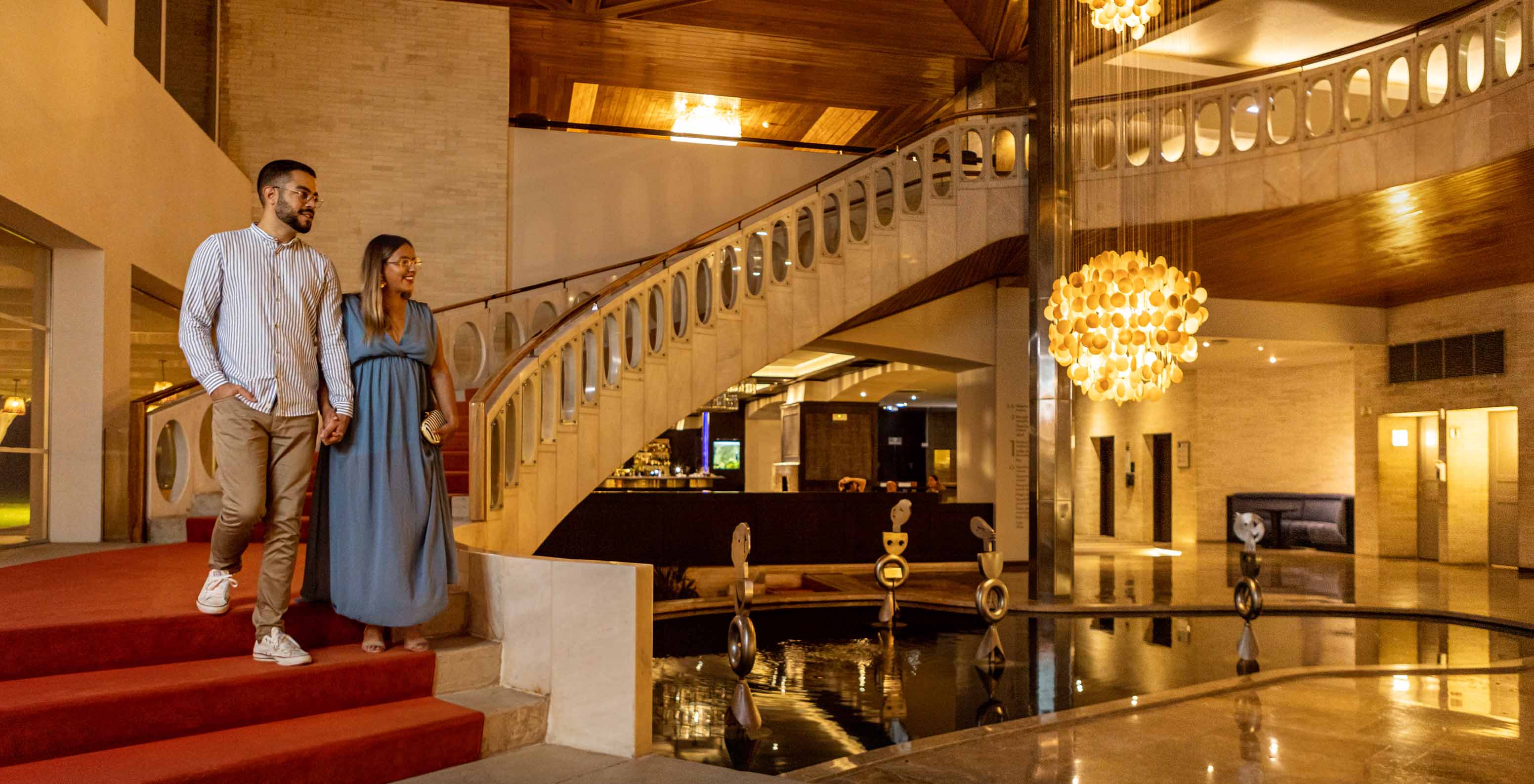 Smiling couple descends the stairs of the lobby at Pestana Alvor Praia, Hotel with Spa and Pool