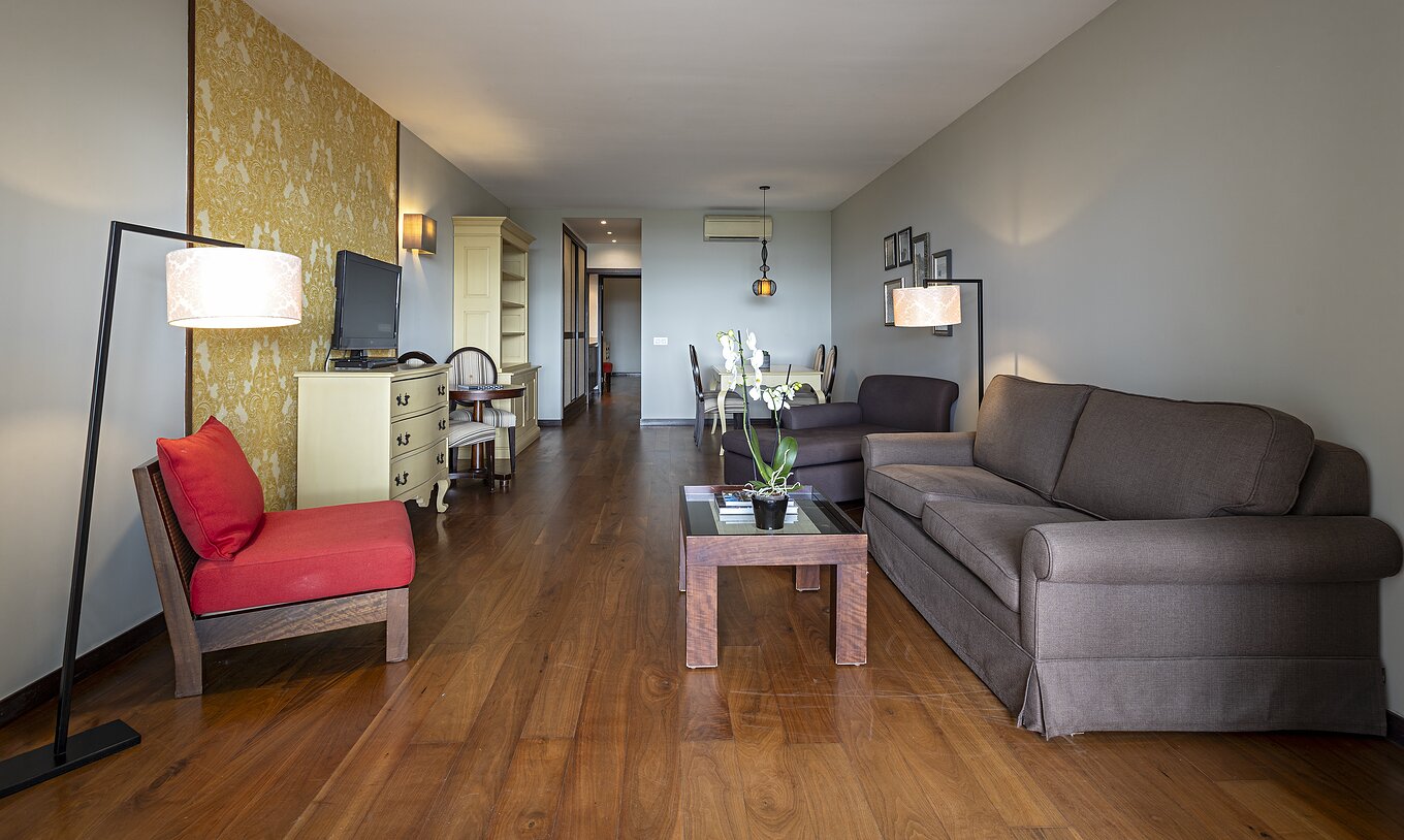 The Cliff Suite T2 at Pestana Alvor Praia has a living room with two sofas, wallpaper, a television, and a table