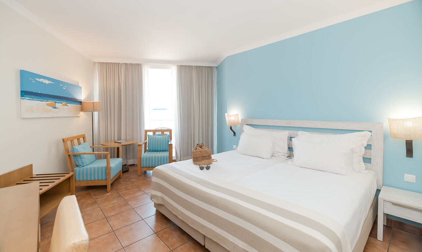 The Deluxe Side Sea View at Pestana Viking has two beds, bedside table and two armchairs by the window