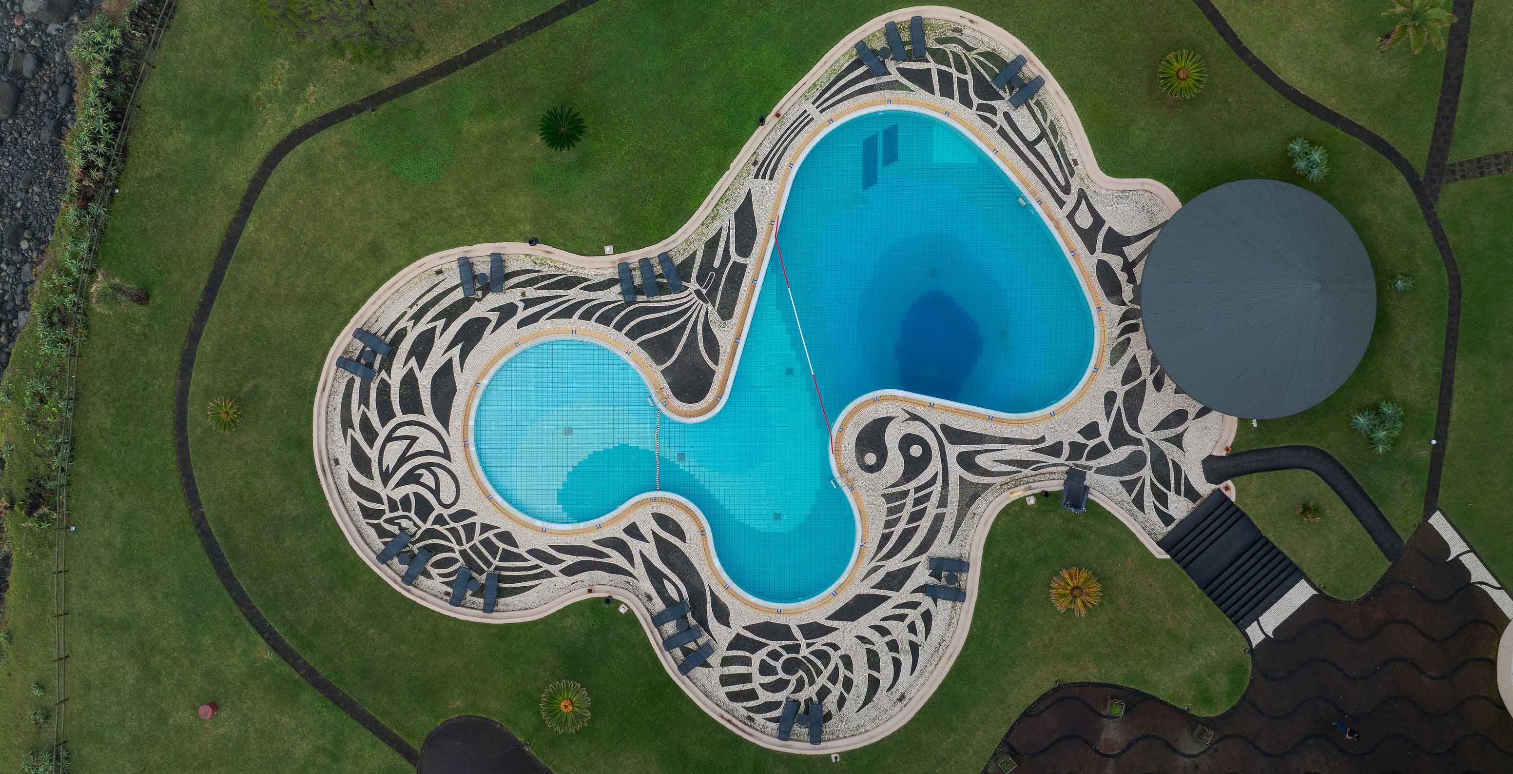Aerial view of Pestana Bahia Praia pool with organic design, surrounded by green lawn and round structure
