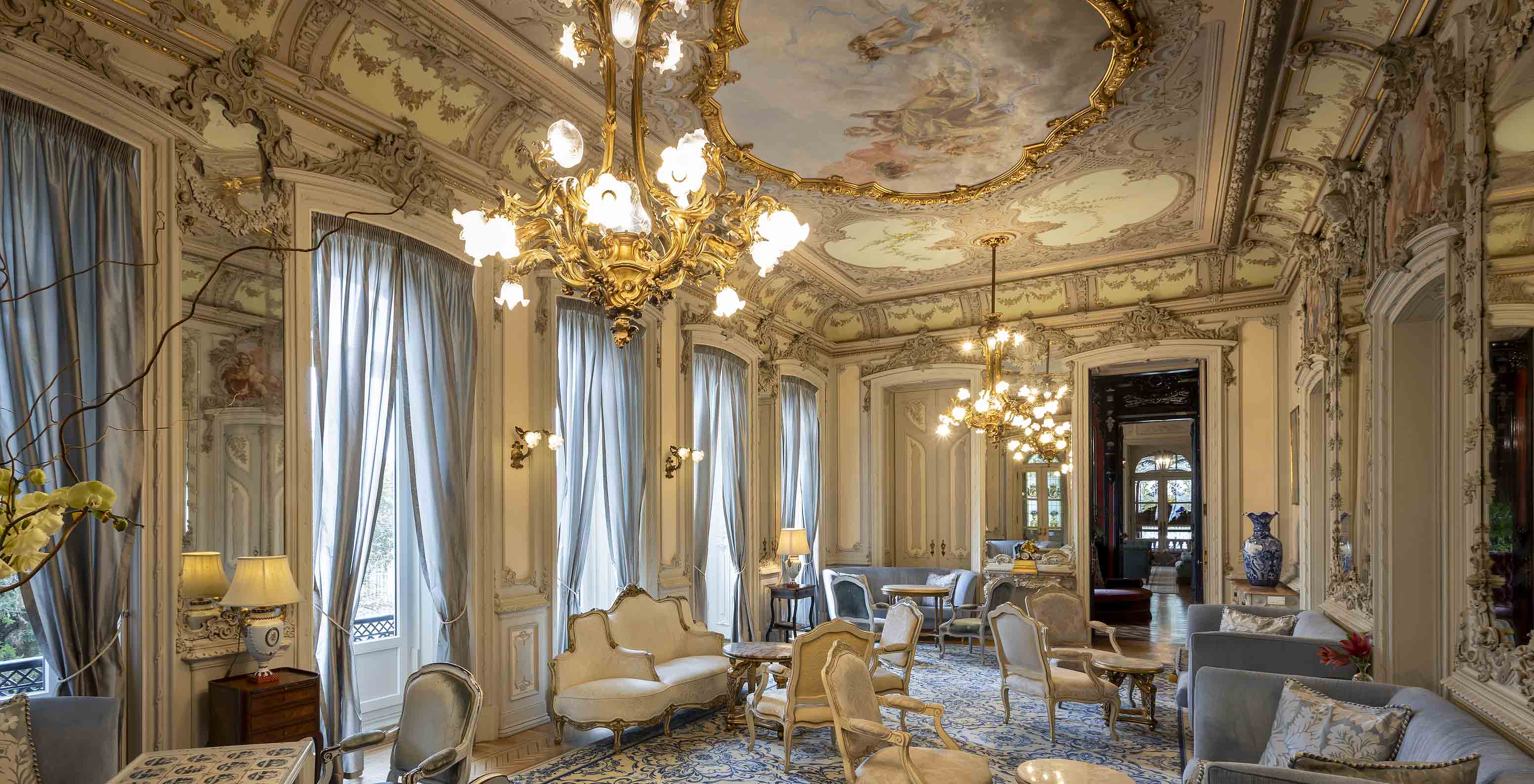 Pestana Palace Lisboa has a palace lounge with ornate walls and ceiling, along with blue armchairs and sofas.