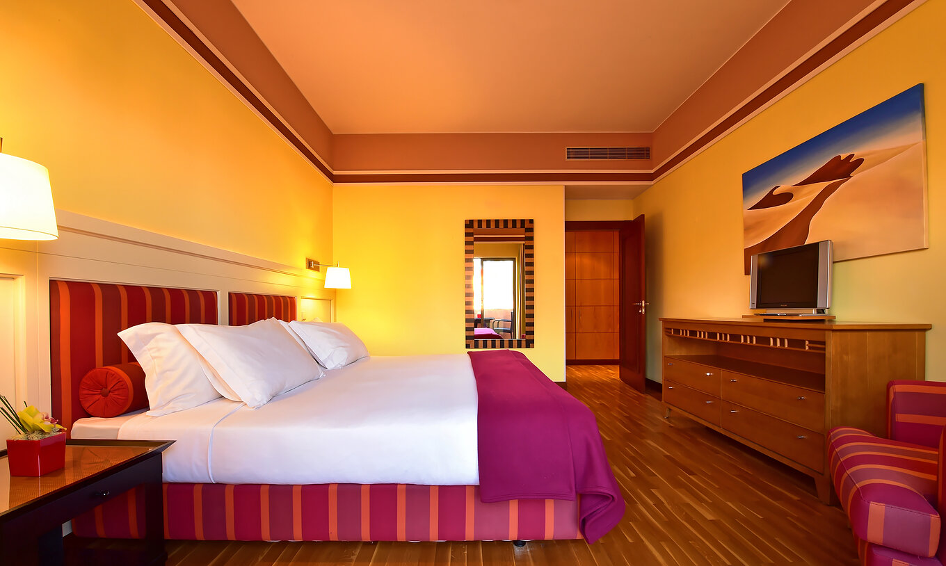 The Superior Suite of Pestana Sintra Golf has a double bed, a mirror on the wall, and a unit with a small television