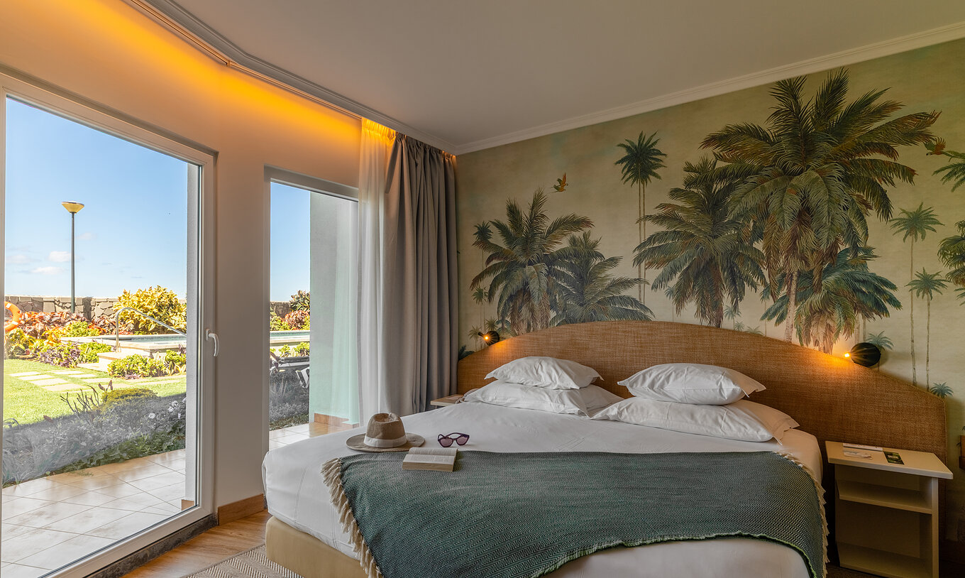 The Pestana Ocean Bay All Inclusive Junior Suite Sea View has a double bed with a green bedspread and wallpaper