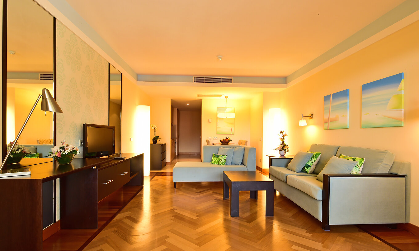 The Suite of Pestana Promenade has a living room with two sofas, a television, mirrors, and hanging paintings