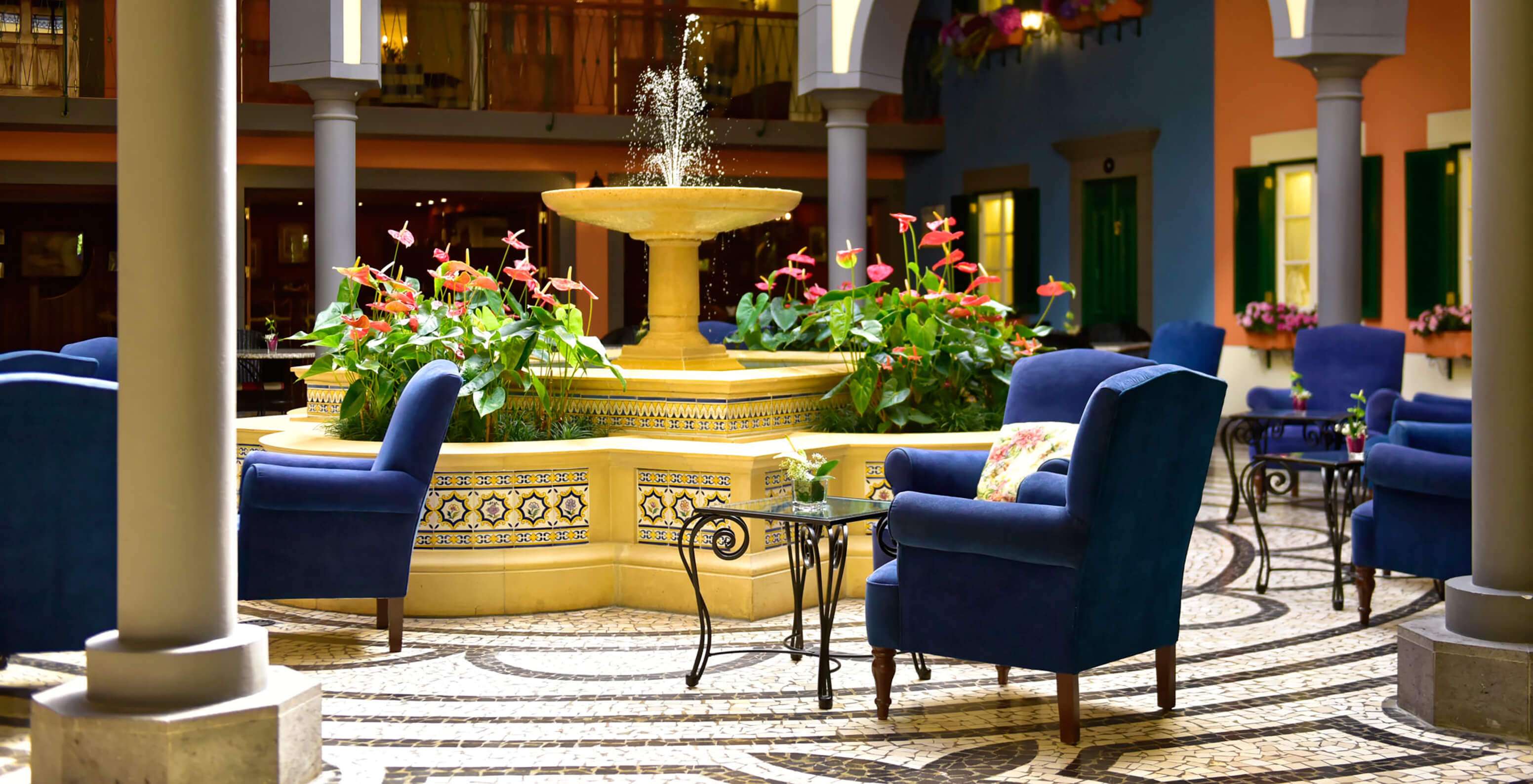 Courtyard with central fountain, pink flowers, blue armchairs at Pestana Village, Hotel with Pool in Funchal