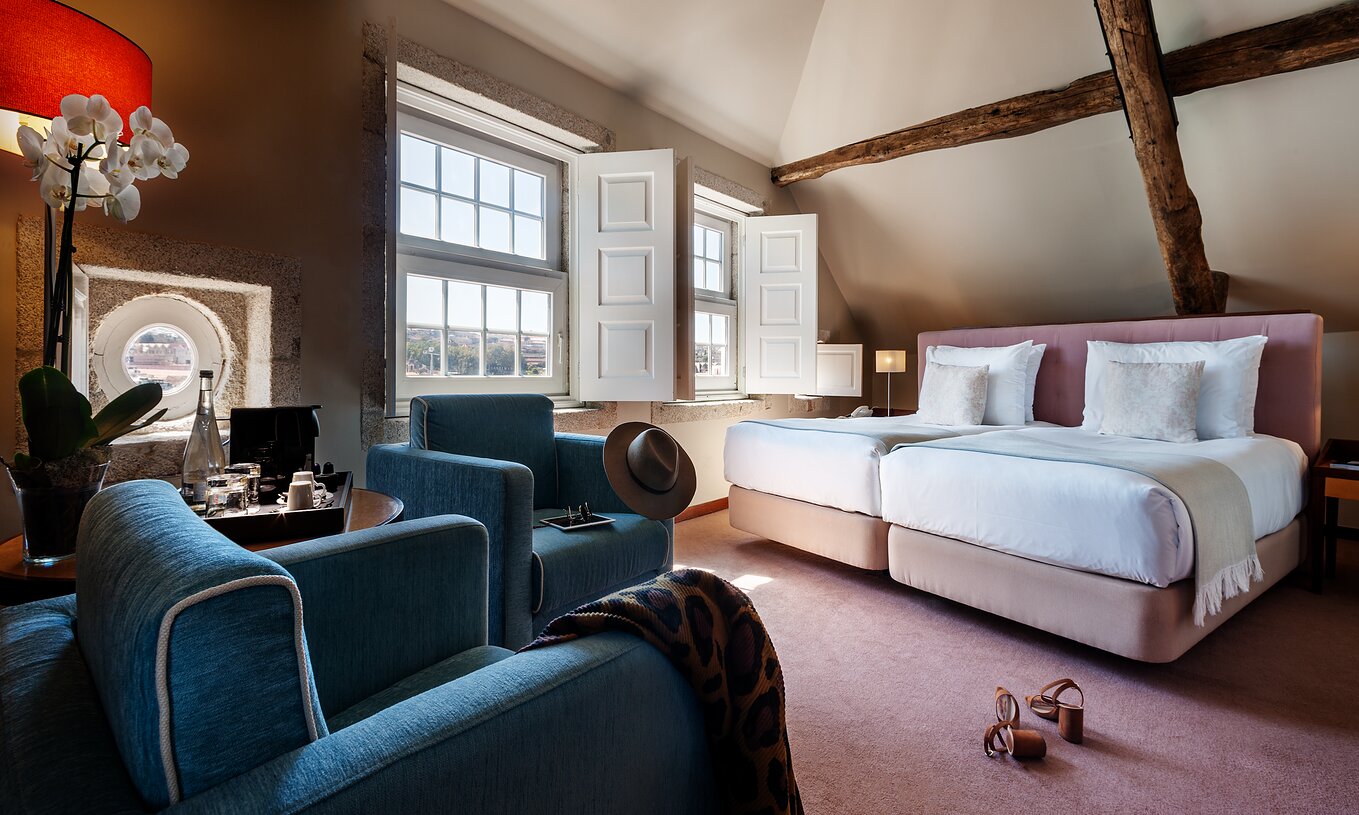 The Plaza room at Pestana Vintage Porto has two beds, two armchairs, a wooden beam on the ceiling and two large windows