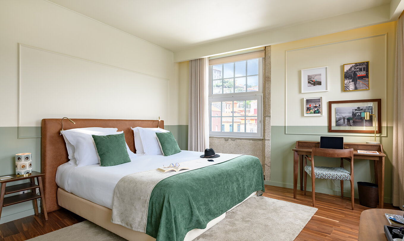 The Vintage Grand View room at Pestana Vintage Porto has a double bed with a green bedspread, a desk and large windows