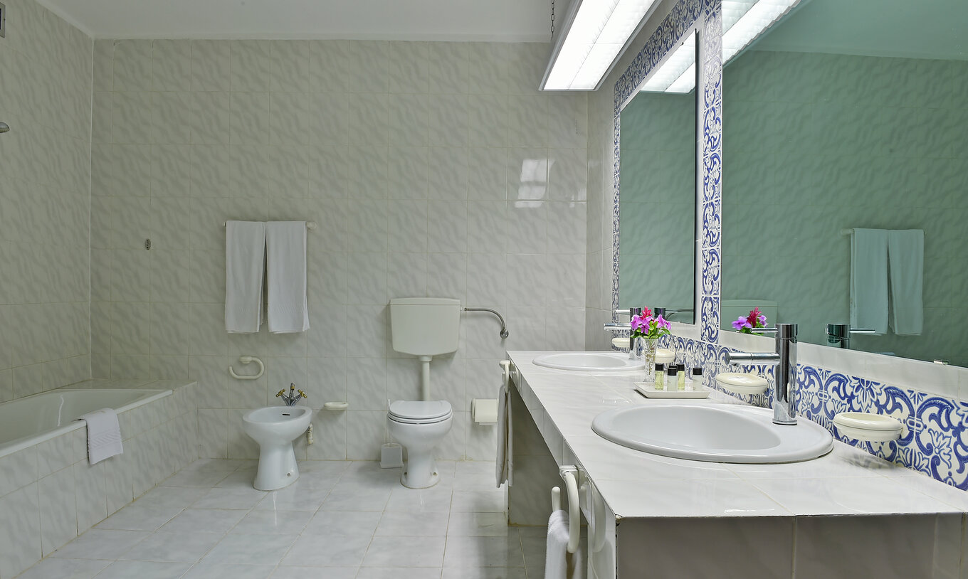 The Standard room at Pestana Miramar São Tomé features a bathroom with tiled walls, two sinks, mirrors, a bidet, and a toilet