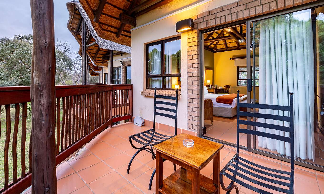 The Standard Room at Pestana Kruger Lodge has a balcony with wooden details, two chairs and a side table