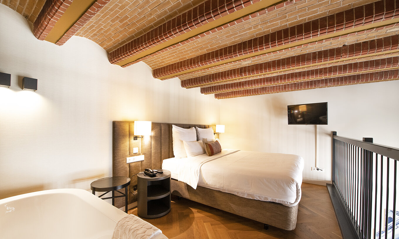 Mezzanine Suite at Pestana Amsterdam Riverside has a double bed, with bedside table, and red brick ceiling