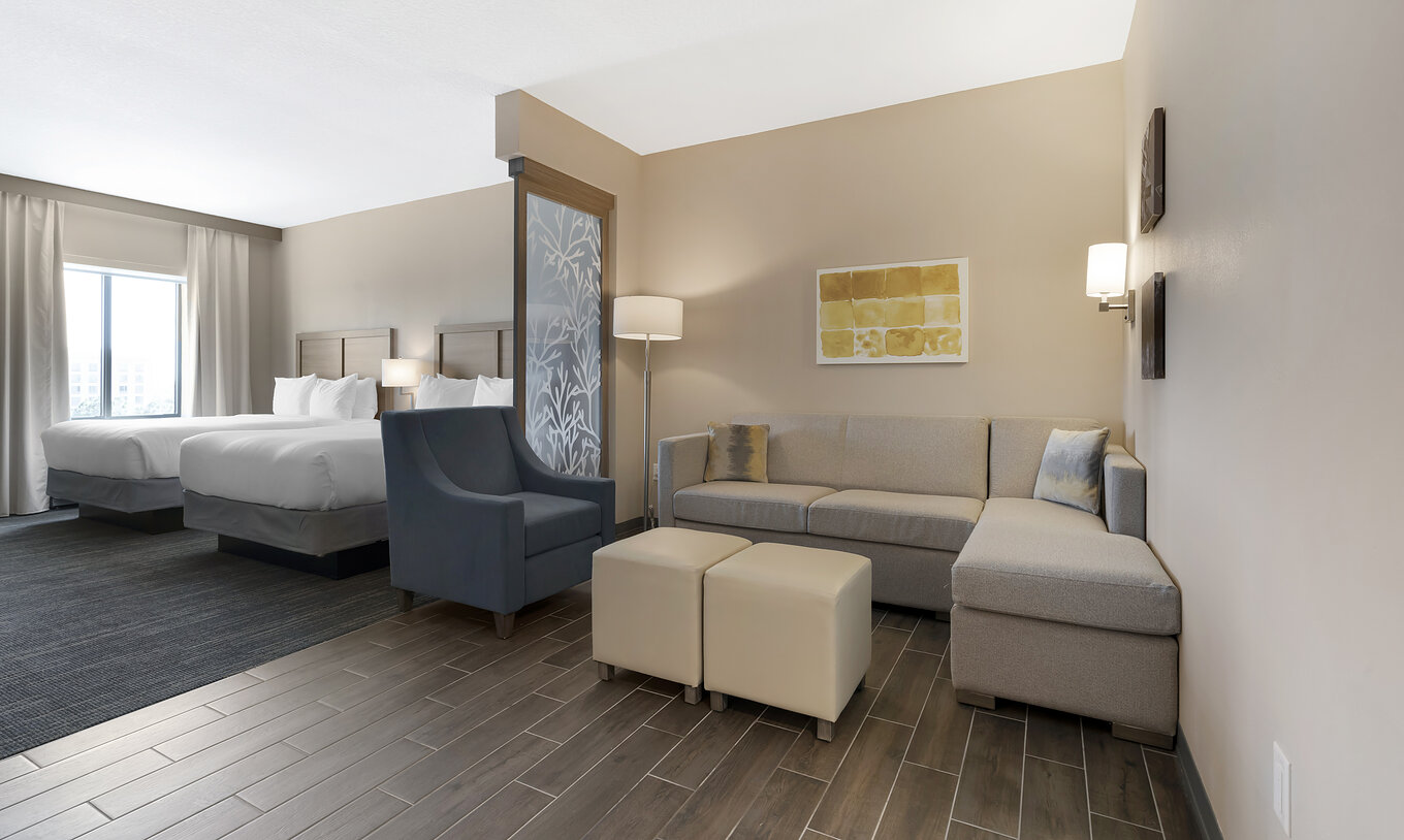 The Superior Double Queen Suite at Pestana Orlando Suites Lake Buena Vista includes two double beds, a sofa, and an armchair