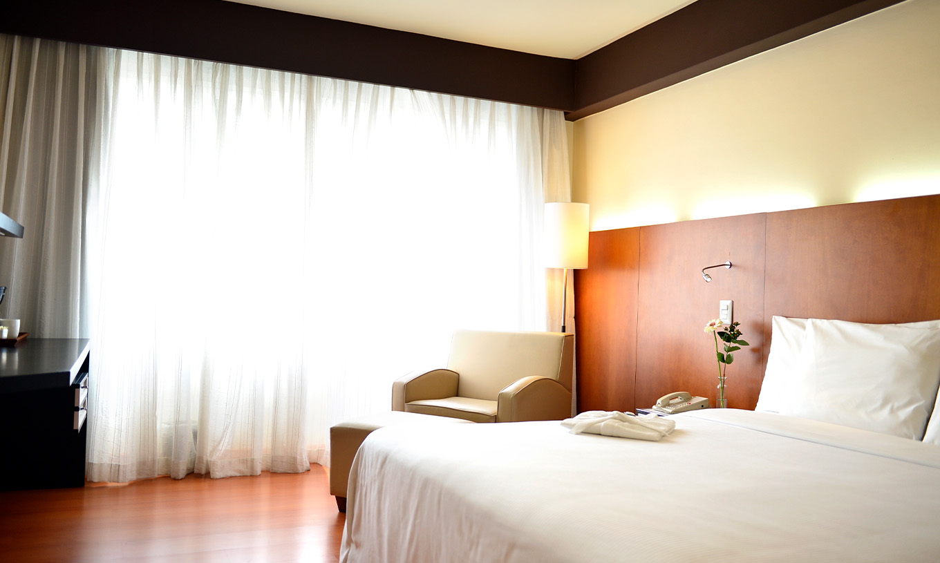 The Executive King Room at Pestana Caracas has a double bed with a wooden headboard and a window with curtains