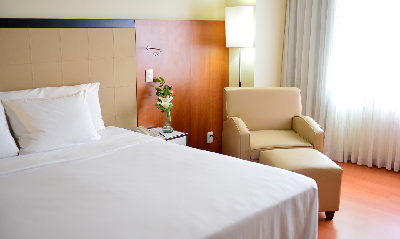 The Twin Executive Room at Pestana Caracas has a double bed, a flower on the bedside table, and a comfortable beige armchair