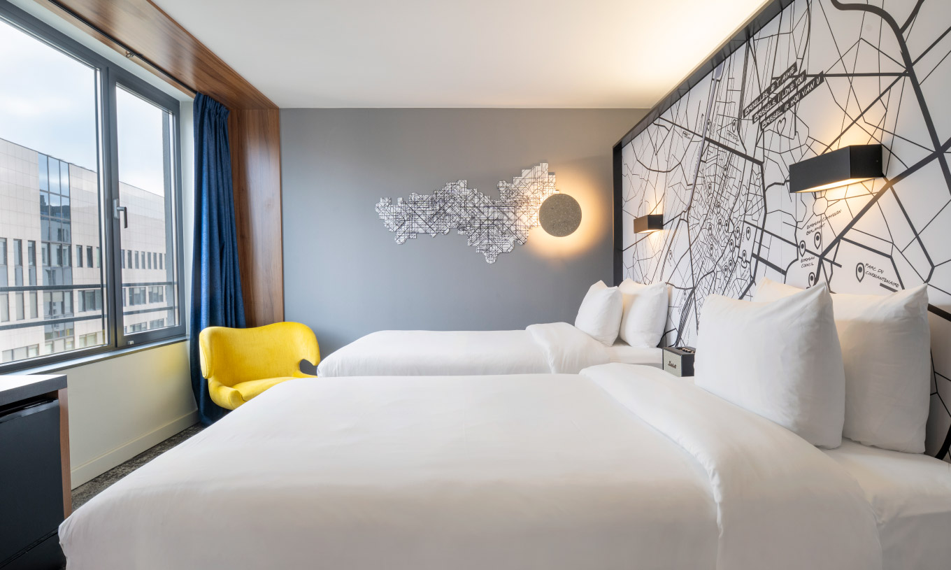 The Superior Twin at Pestana Brussels Schuman has two single beds, a yellow chair, and a window with a view