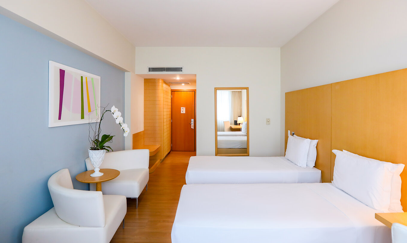 The Twin Standard at Pestana Curitiba has two single beds with sofas at the foot of the bed and a small table with flowers
